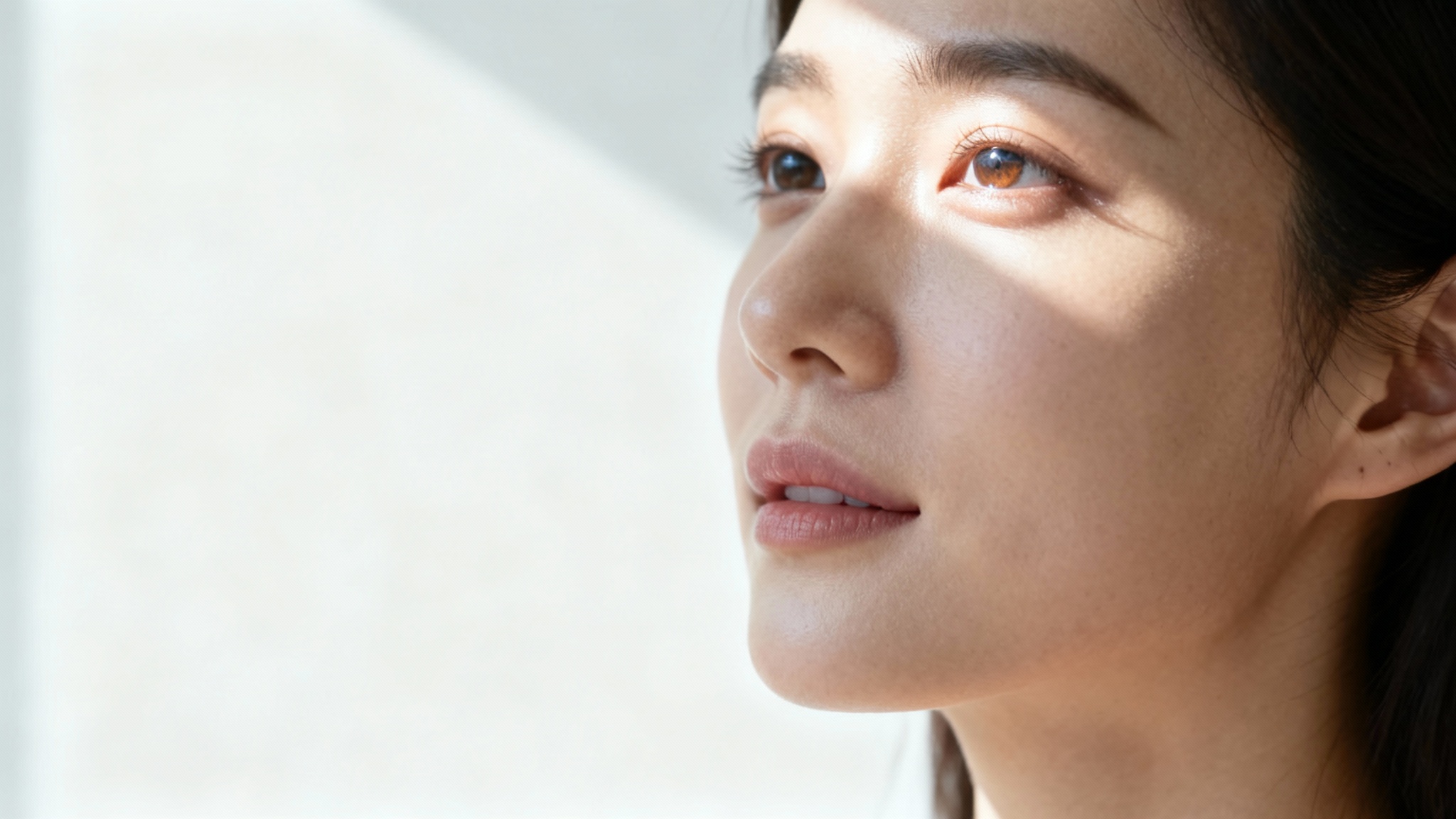 A photorealistic portrait of a woman's face softly illuminated by natural light from a window, set against a plain white background, exemplifying natural light portraiture.