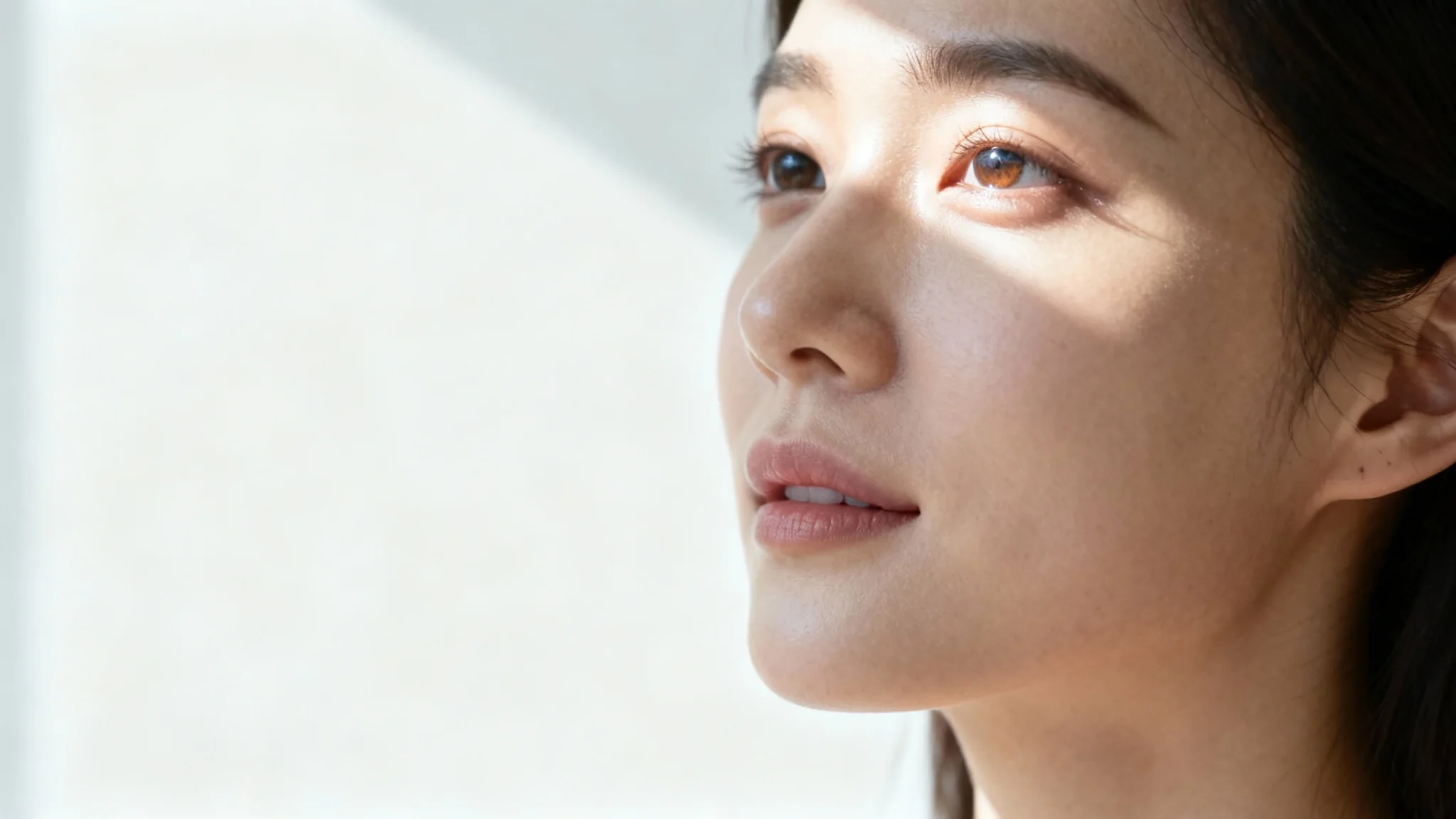 A photorealistic portrait of a woman's face softly illuminated by natural light from a window, set against a plain white background, exemplifying natural light portraiture.