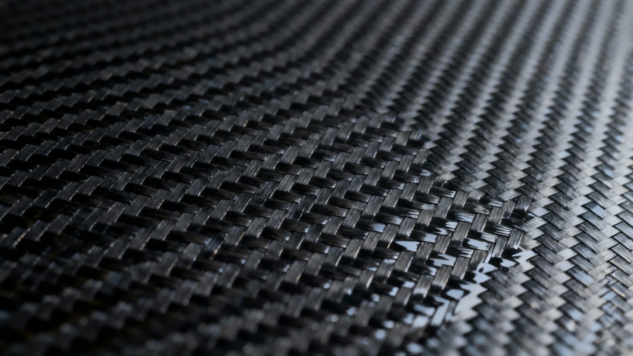A close-up, high-resolution image of a sleek, glossy carbon fiber texture, showing the intricate diagonal weave pattern reflecting light on its dark, modern surface.