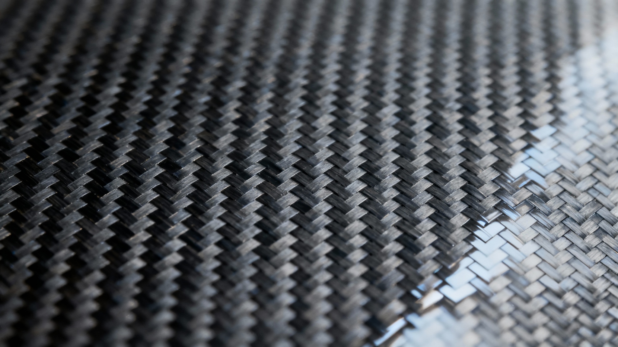 A detailed, close-up macro shot of a glossy carbon fiber texture, showing the intricate black and gray woven pattern and reflective surface.