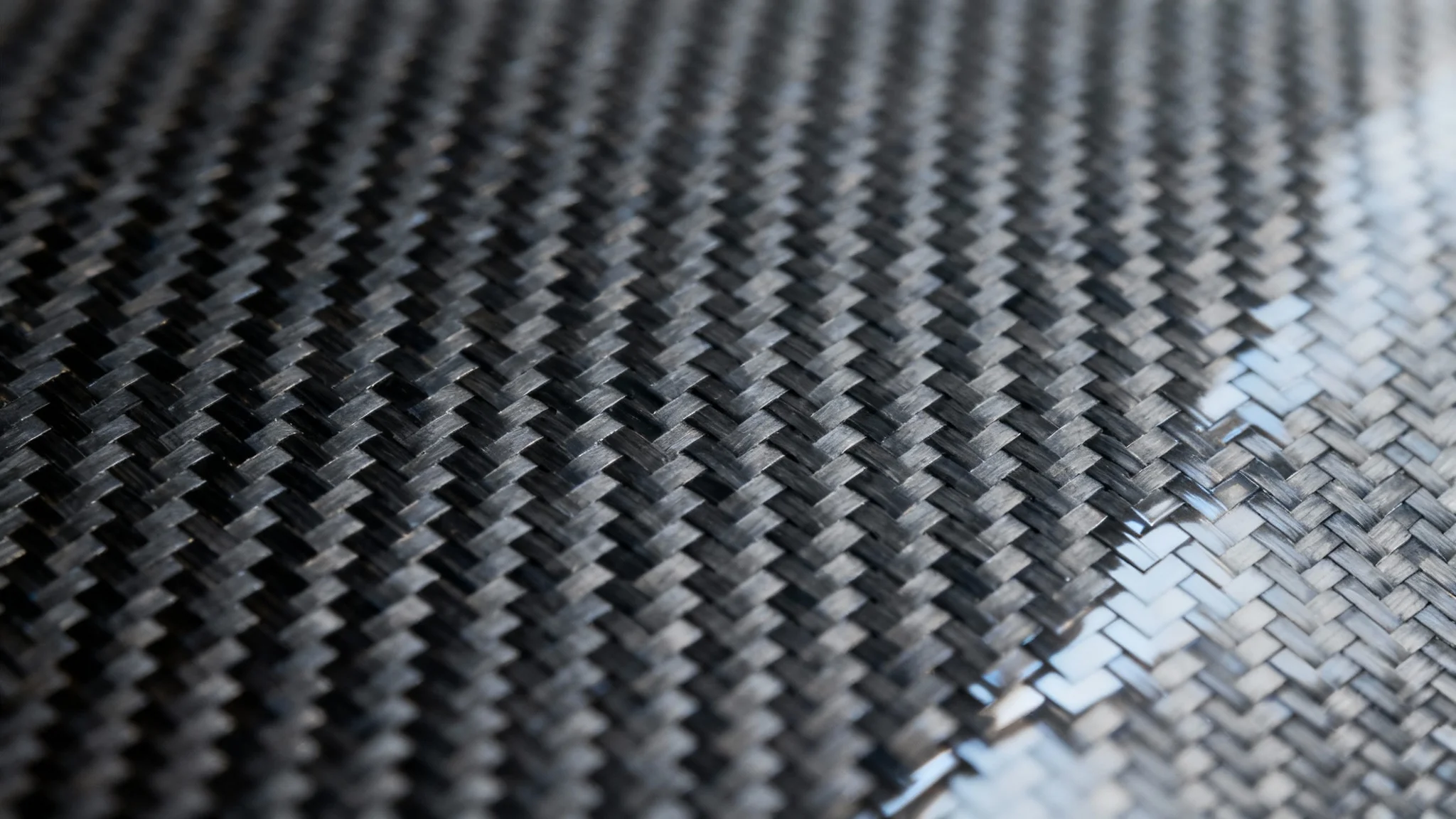 A detailed, close-up macro shot of a glossy carbon fiber texture, showing the intricate black and gray woven pattern and reflective surface.