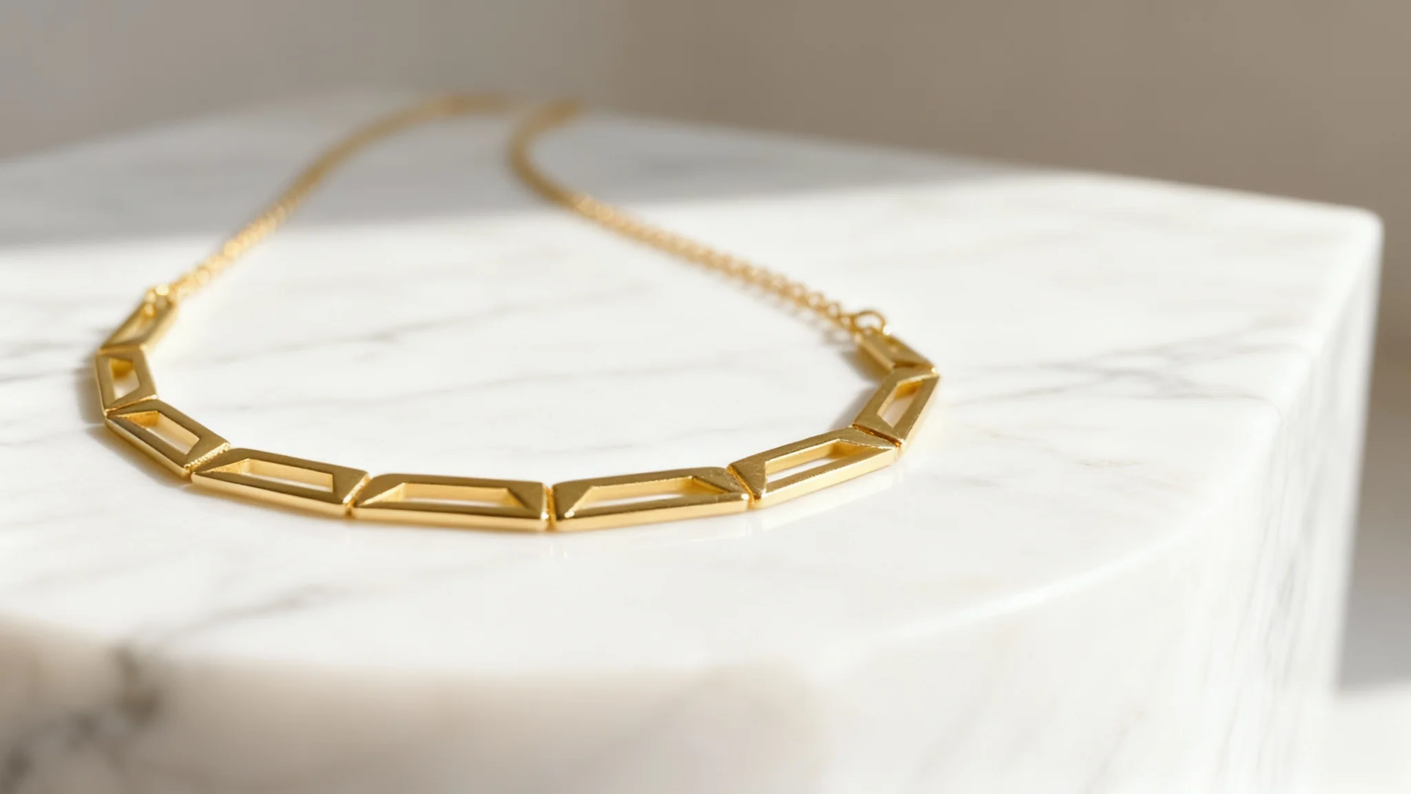 A close-up, professional product photograph of a modern gold necklace with geometric patterns, artfully placed on a white marble surface under soft studio lighting.
