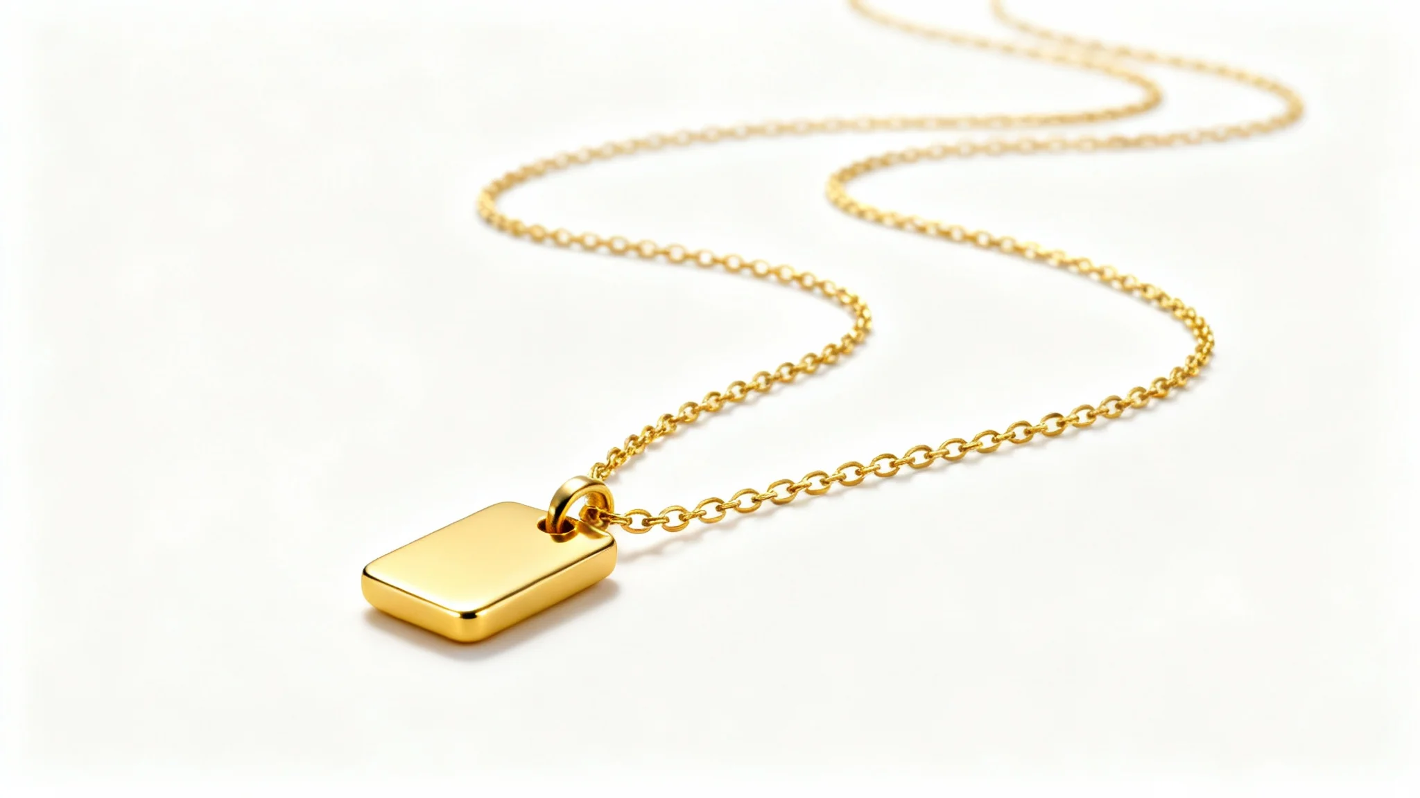 A professional product photograph of an elegant, minimalist gold necklace with a delicate chain and a polished pendant, set against a clean white background.