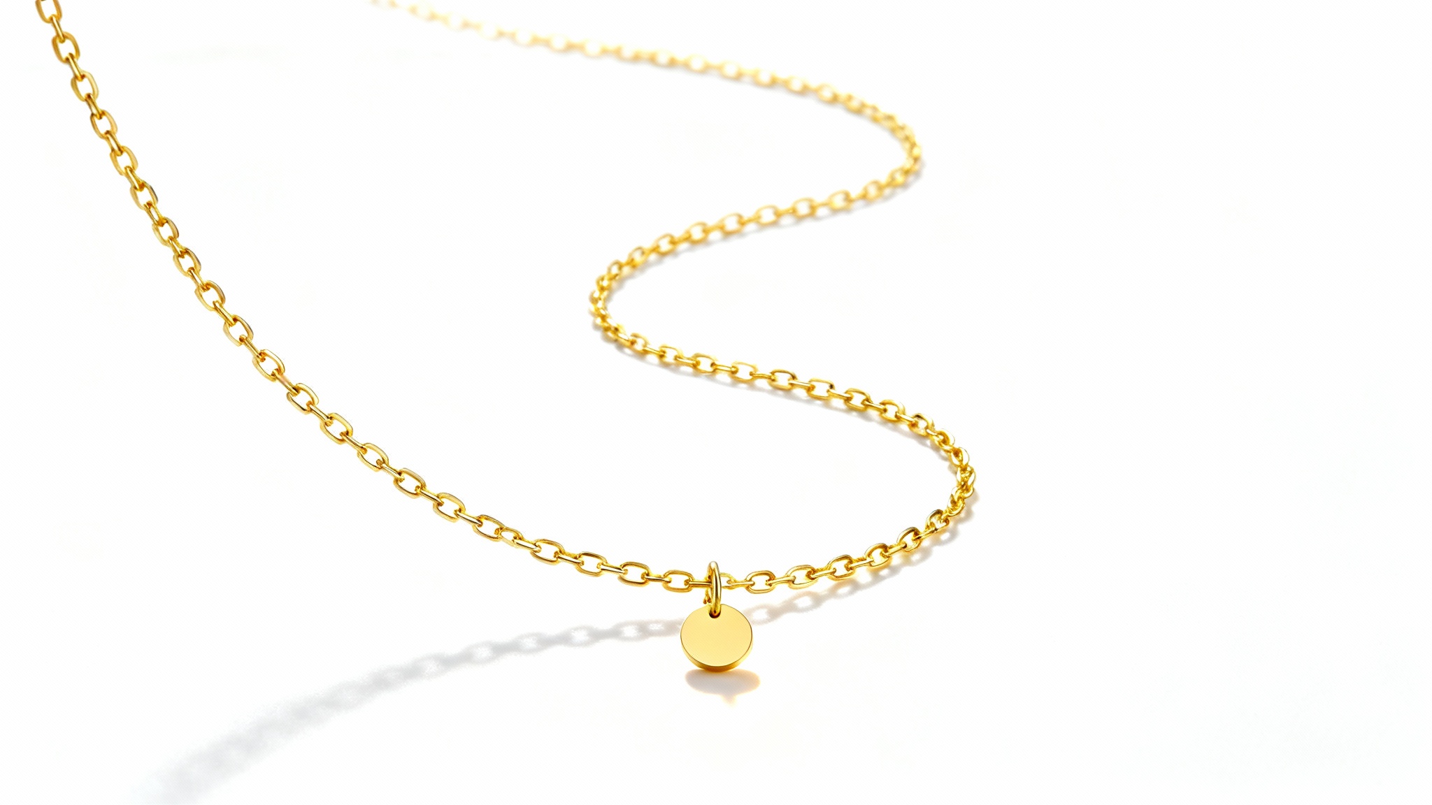 A professional product photograph of a delicate gold necklace with a small, round pendant, elegantly arranged on a clean white background to highlight its luxury.