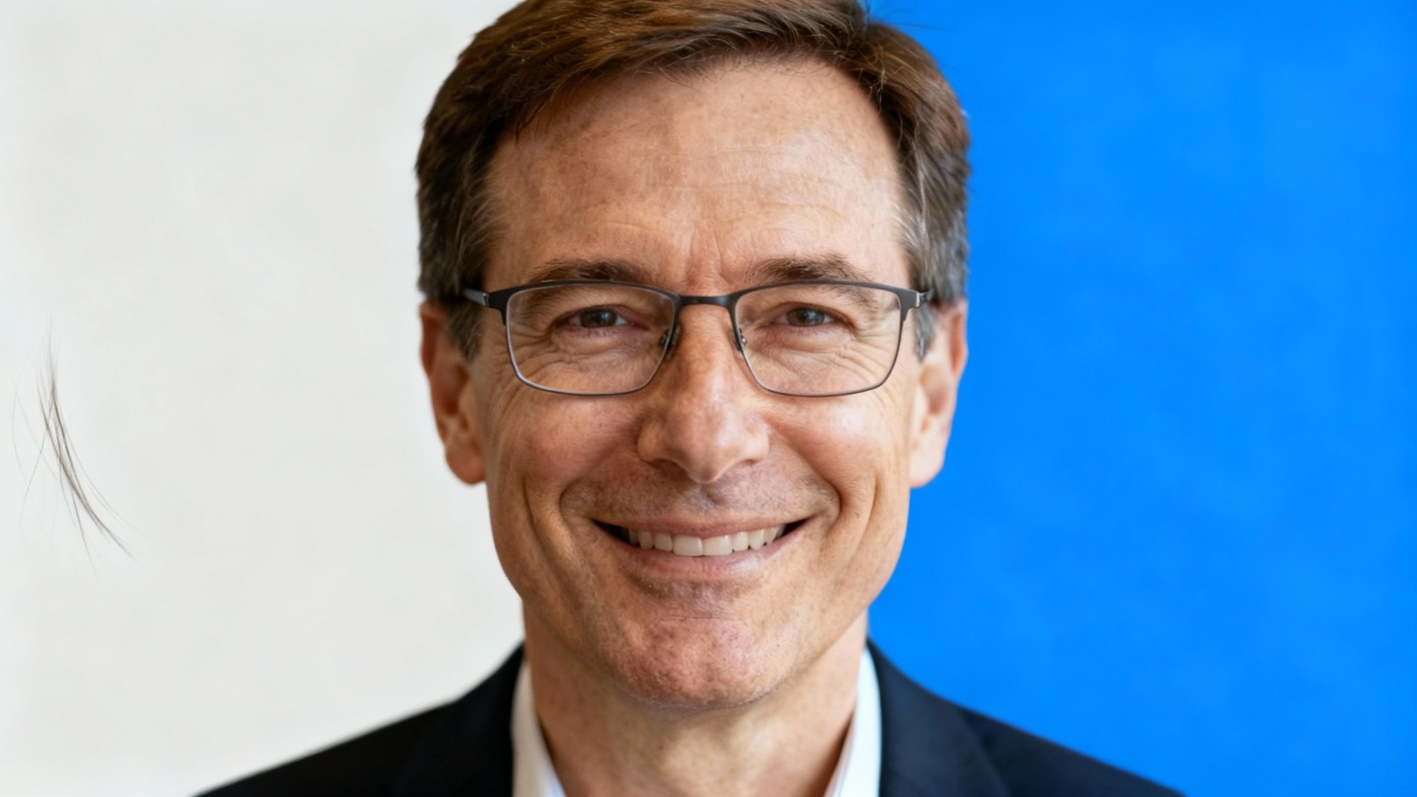 A professional headshot of a smiling man with glasses, perfectly cut out and placed over a split-color gray and blue background to demonstrate a transparent background feature.