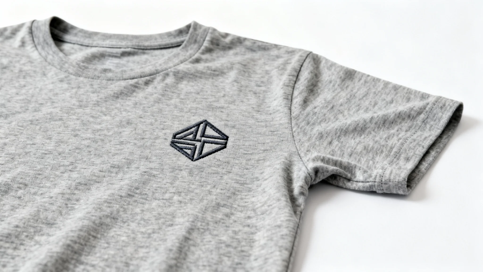 A close-up shot of a minimalist abstract logo embroidered in dark thread on the chest of a heather gray t-shirt, displayed against a plain white background.