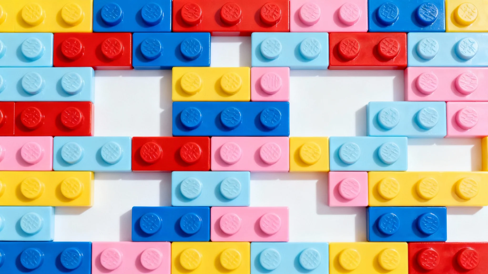 A flat-lay, top-down photograph of a colorful background made of interconnected plastic toy bricks in various vibrant colors, presented on a clean white background.