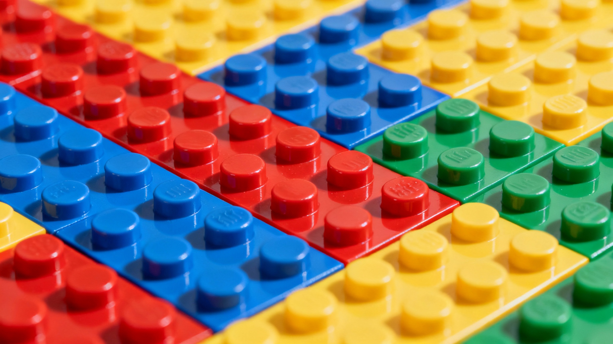 A close-up, top-down view of a colorful background made of interlocking toy building bricks in various primary colors, creating a textured and vibrant pattern.