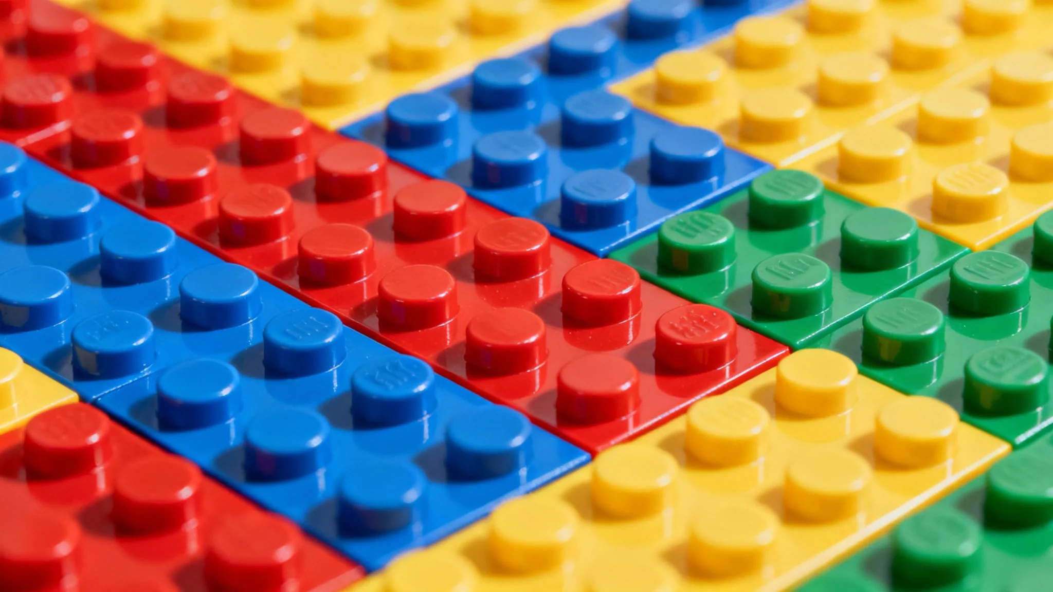 A close-up, top-down view of a colorful background made of interlocking toy building bricks in various primary colors, creating a textured and vibrant pattern.