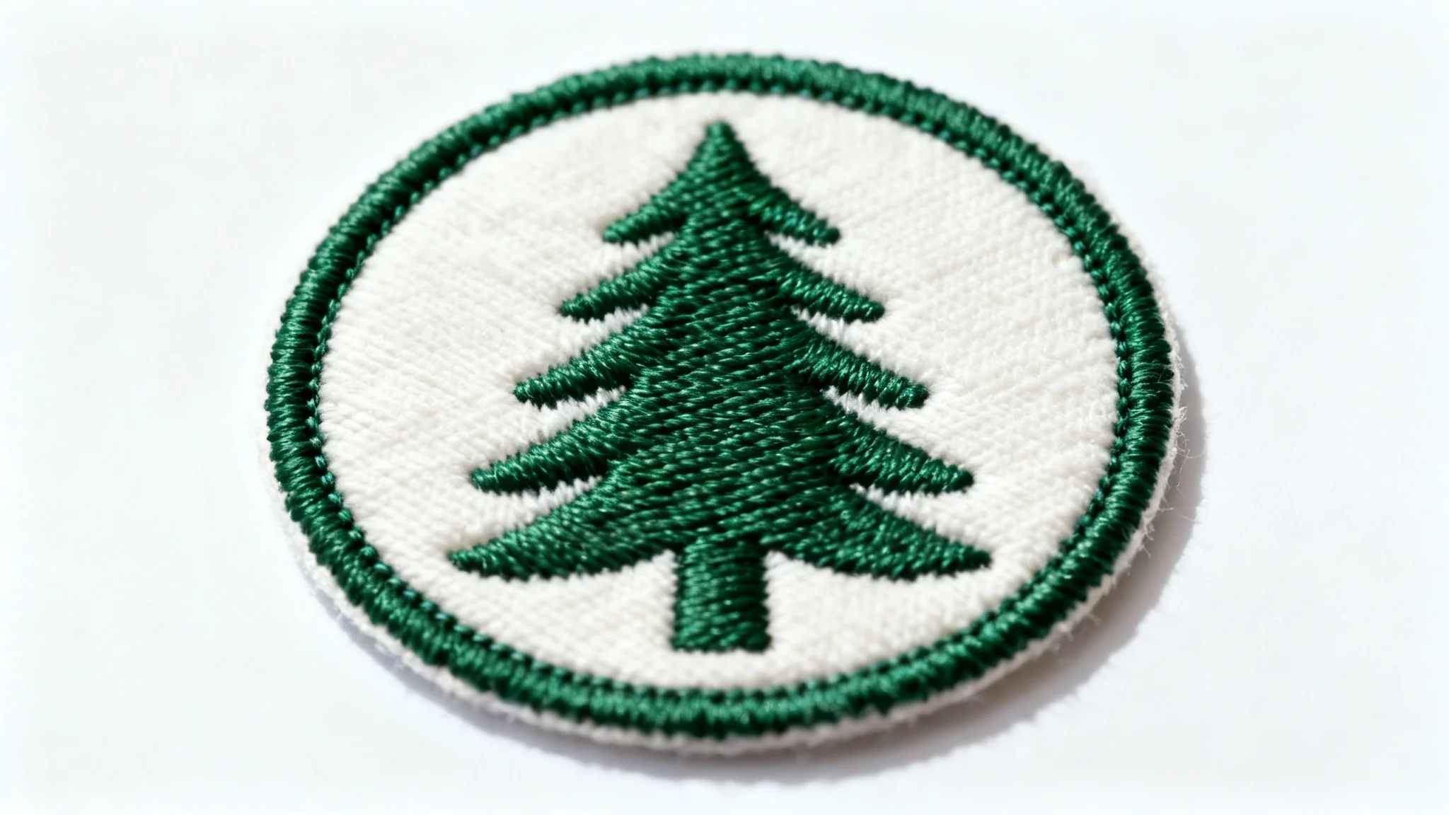 A photorealistic mockup of a circular embroidered patch with a logo of a stylized green pine tree, isolated on a white background to highlight the detailed stitching and thread texture.