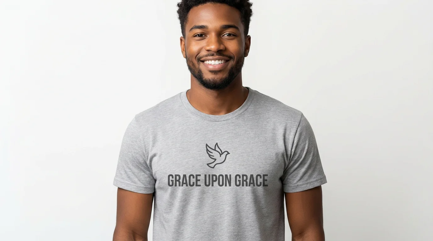 A smiling young man modeling a heather gray gospel t-shirt against a clean white background. The shirt has a minimalist design with a dove icon and the words 'GRACE UPON GRACE' printed on it.