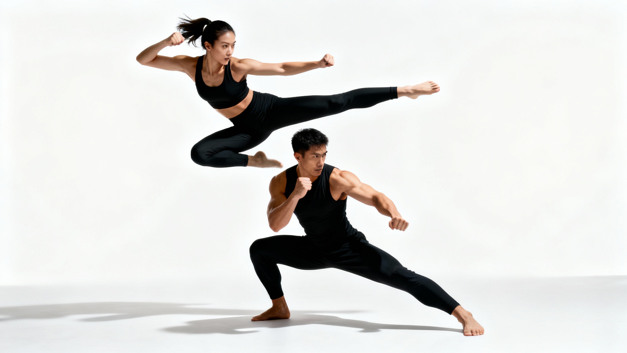 A man and a woman demonstrating a duo fighting pose against a clean white background. The woman is captured mid-air in a side kick while the man crouches beneath her in a defensive stance.
