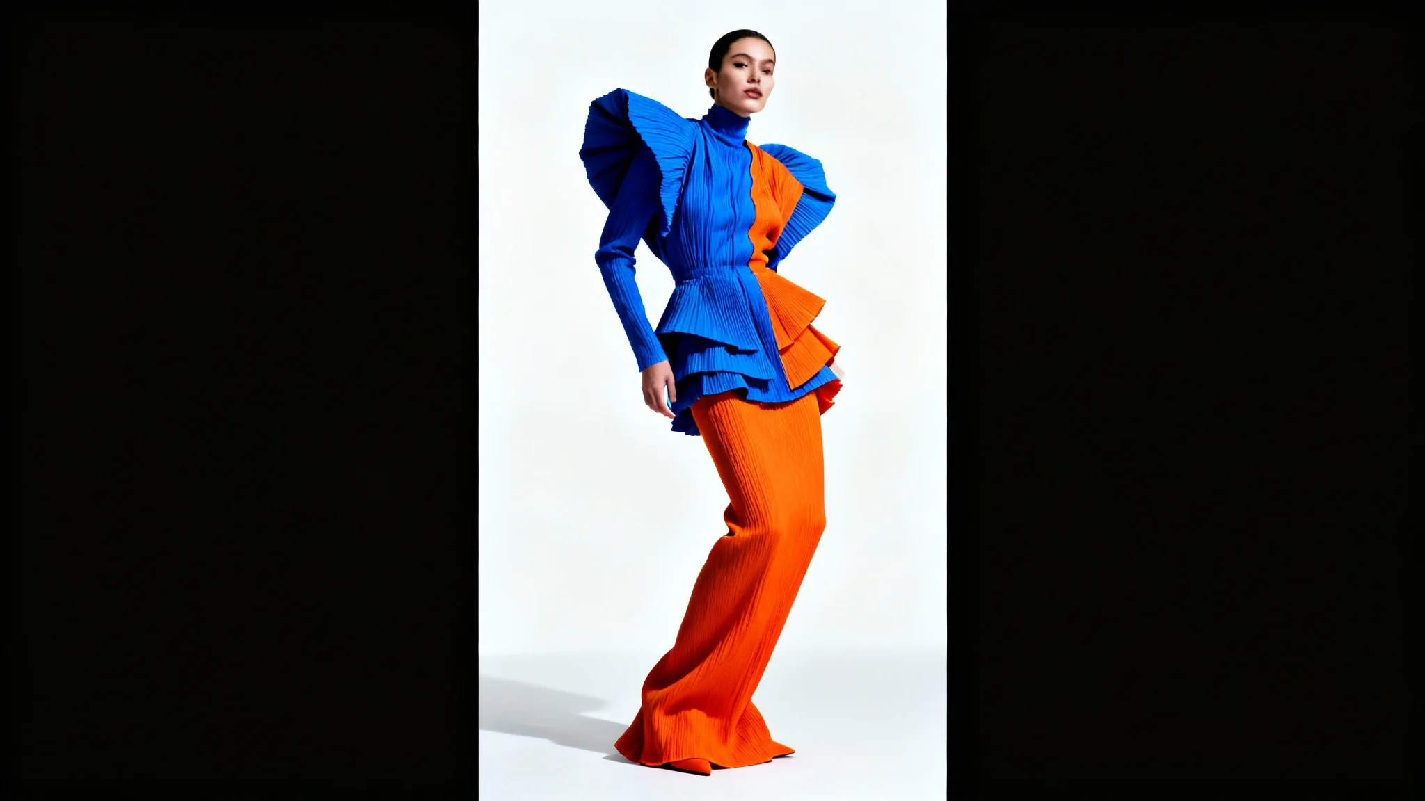 A fashion model posing in a bold, sculptural blue and orange outfit against a clean white background, showcasing a modern and high-fashion design.