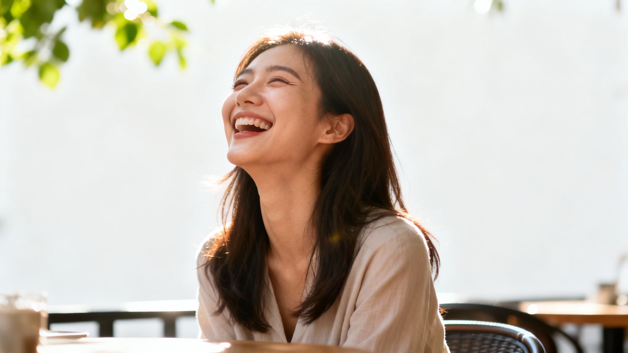 A candid, sunlit photograph of a young woman laughing with pure joy at an outdoor cafe, presented as a clean mockup on a white background.