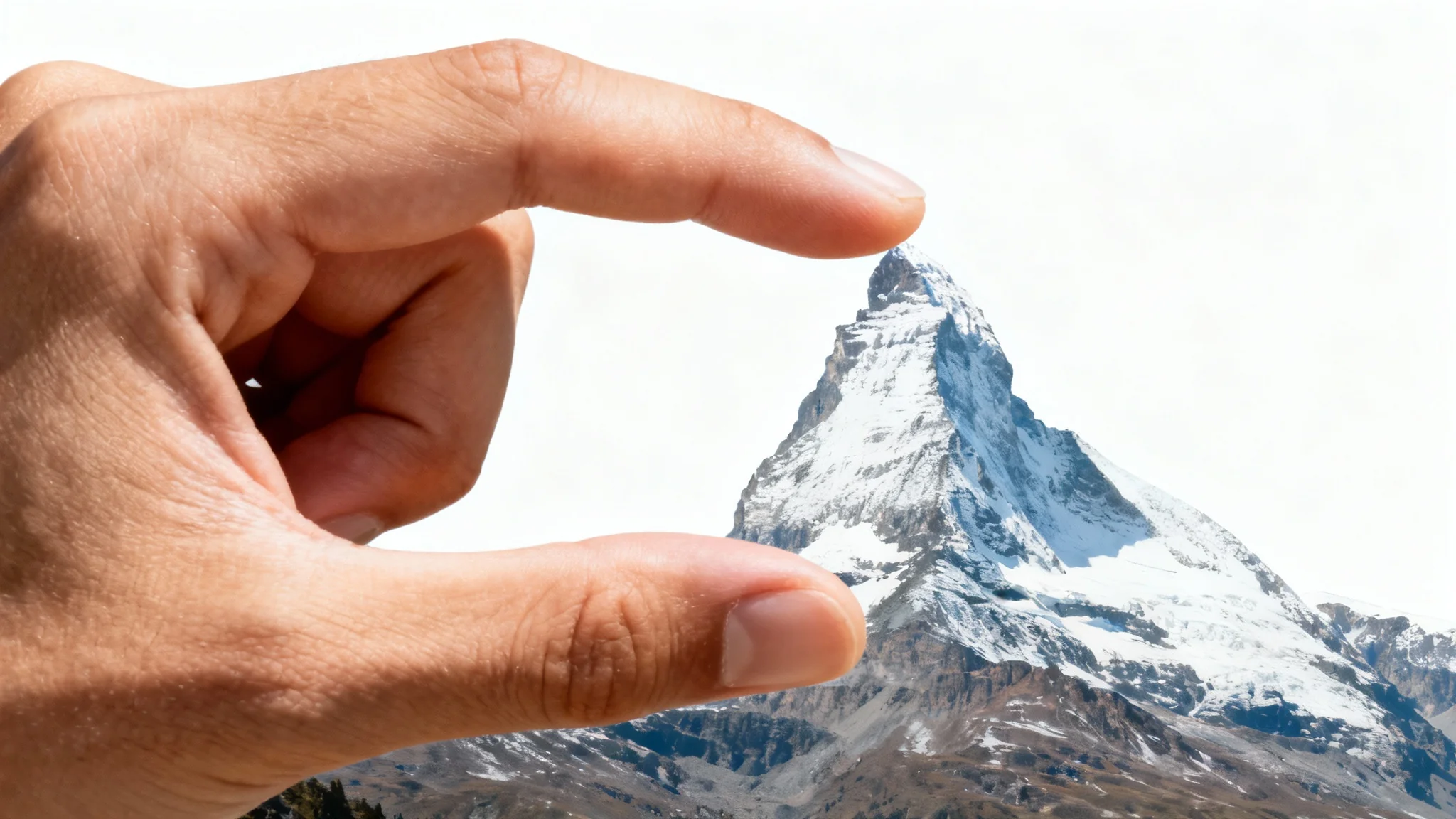 A clever forced perspective photograph where a hand in the foreground appears to be pinching the peak of a distant mountain, demonstrating the creative technique.