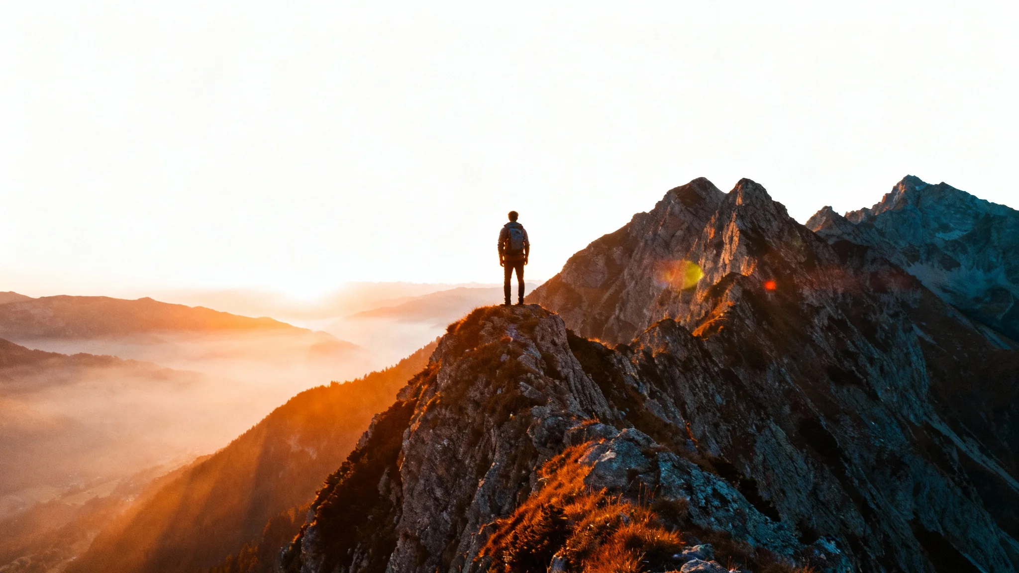 A photorealistic, cinematic still of a lone hiker standing on a mountain peak at sunrise, looking out over misty valleys. The image has a professional, movie-like quality.