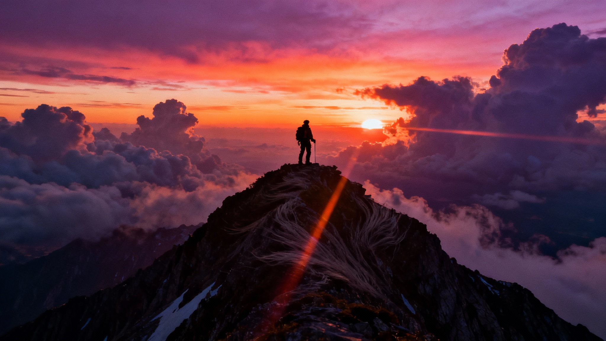 A cinematic, wide-angle shot of a lone figure silhouetted on a mountain peak against a dramatic sunset, evoking the feeling of an epic film.