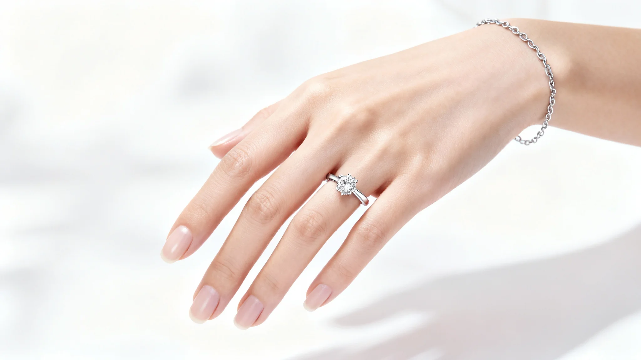 A close-up photo of an elegant hand with a perfect manicure modeling a delicate diamond ring and a matching bracelet against a plain white background.