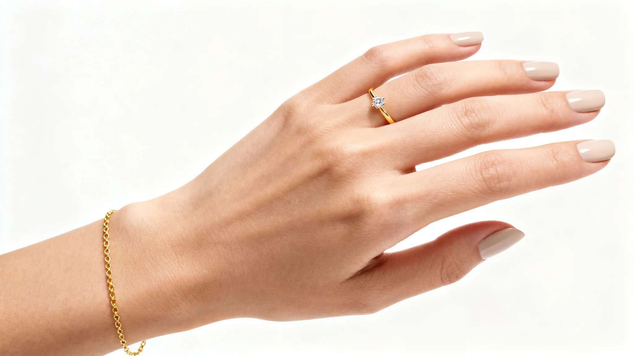 An elegant, manicured hand models a delicate gold ring and a matching thin bracelet against a clean white background, in a professional jewelry photograph.