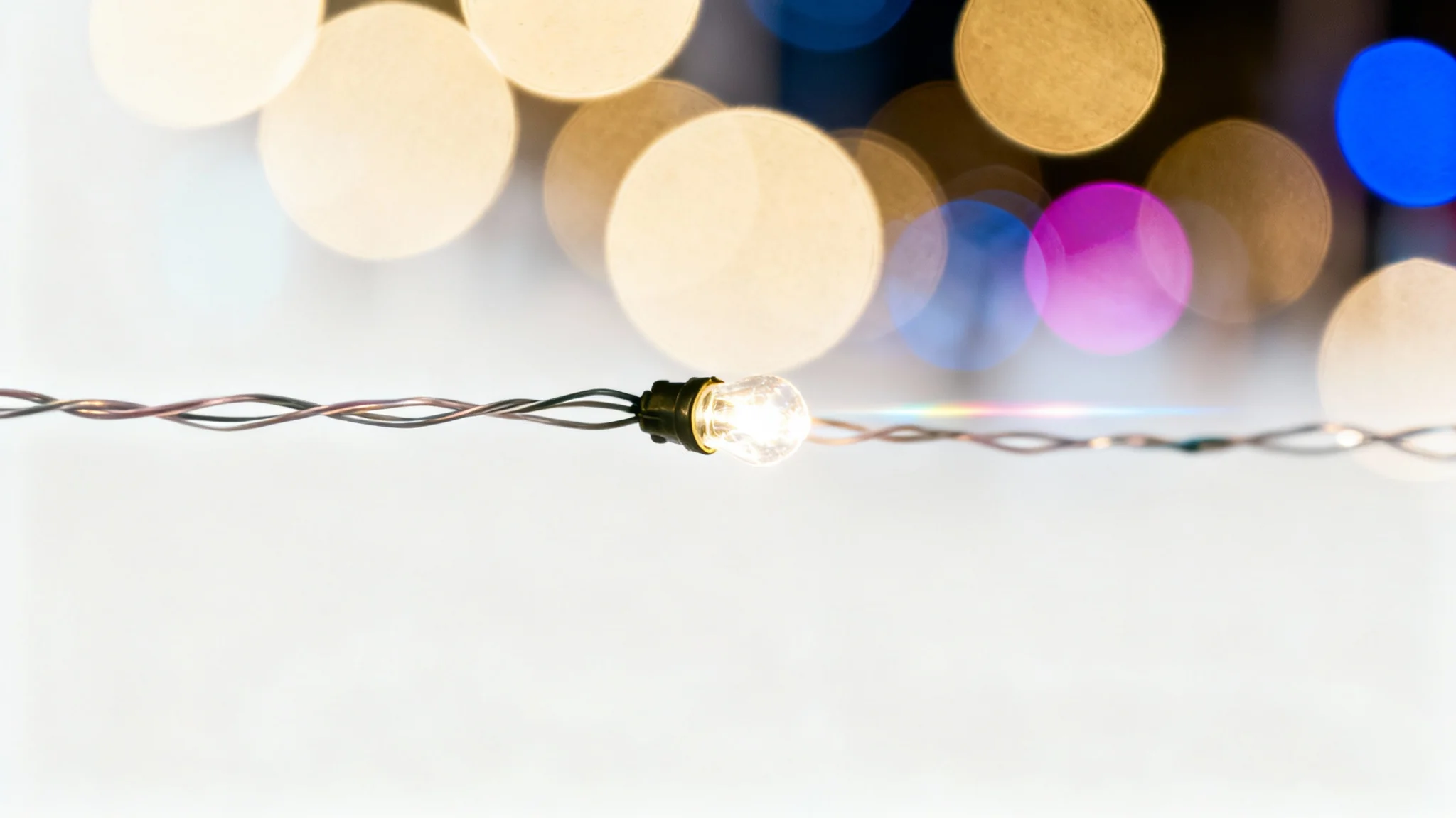 A photorealistic image demonstrating a camera lens effect, with a single fairy light in sharp focus and a background of city lights blurred into large, colorful bokeh circles, all on a clean white background.