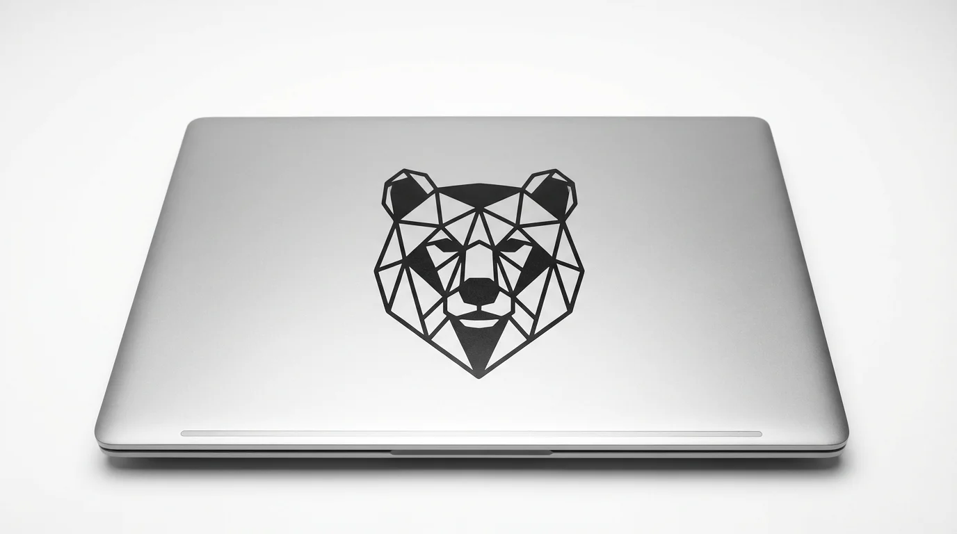 A photorealistic mockup of a matte black vinyl decal of a geometric bear applied to the lid of a silver laptop on a clean white background.