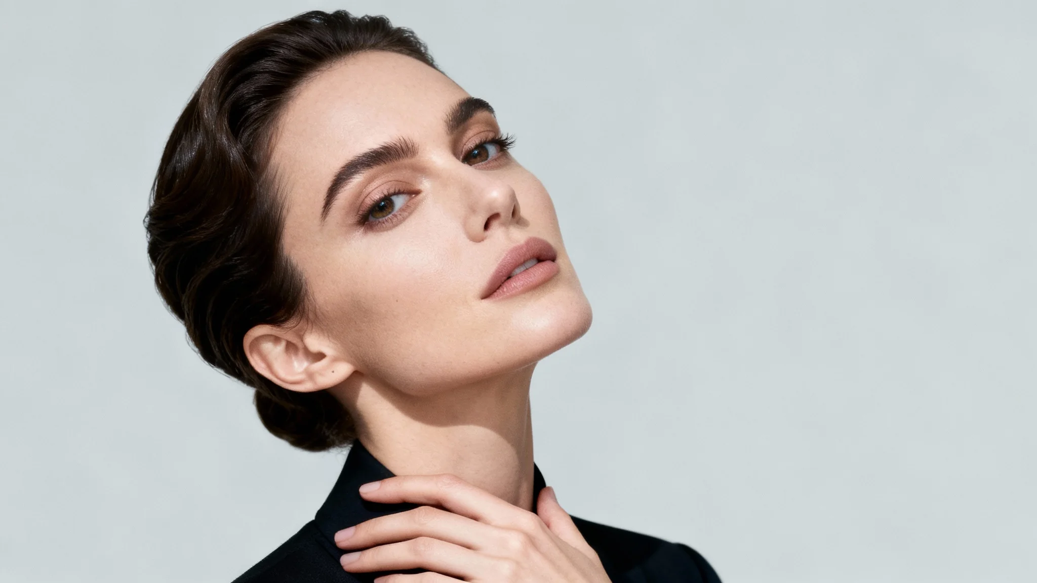 A realistic photograph of a woman in a classic three-quarter portrait pose, looking at the camera against a plain grey studio background. The image serves as a reference for portraiture.