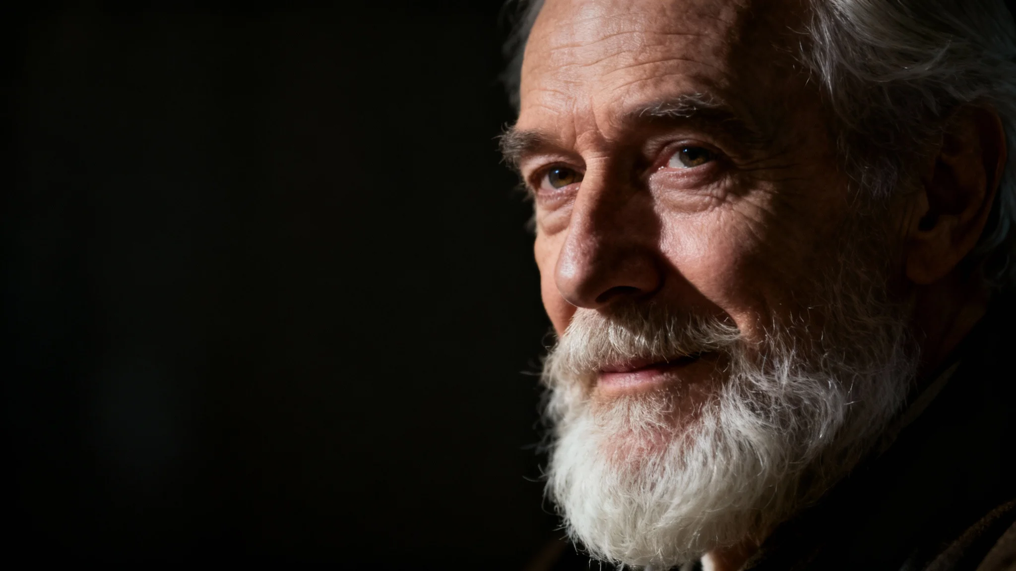 A dramatic, cinematic portrait of an elderly man with a white beard. He is lit with strong side lighting against a dark, blurry background, creating a moody and thoughtful atmosphere.