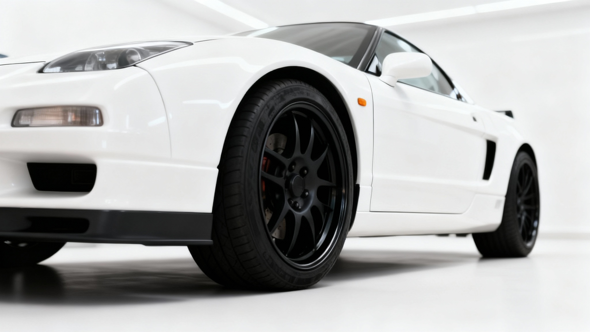 A close-up photograph of a white sports car with perfectly fitted new matte black wheels, parked in a clean, modern studio. The image showcases the ideal result of a wheel fitment customization.