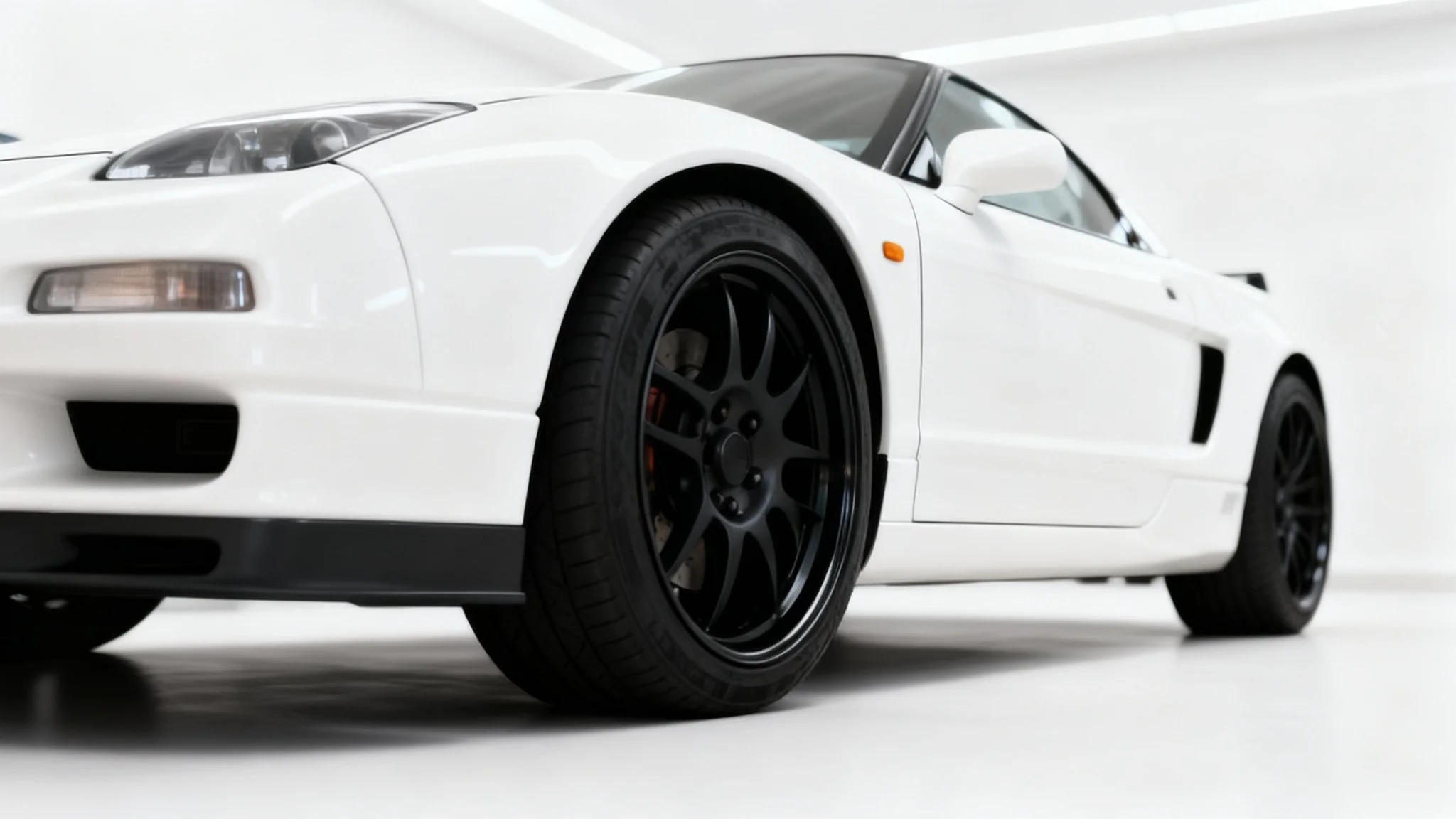 A close-up photograph of a white sports car with perfectly fitted new matte black wheels, parked in a clean, modern studio. The image showcases the ideal result of a wheel fitment customization.