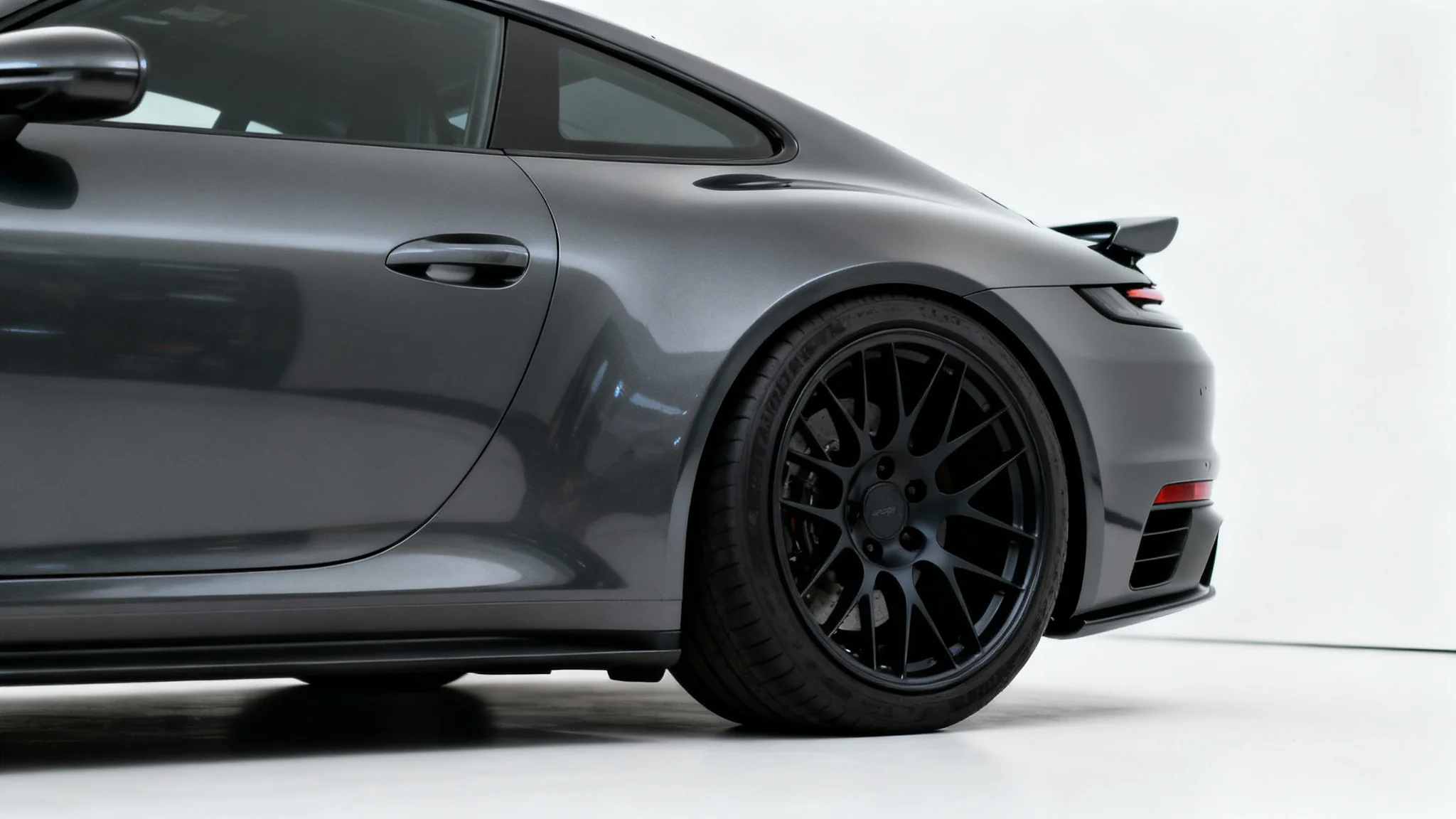 A close-up shot of a charcoal grey sports car's wheel, demonstrating a perfect, flush fitment of a custom matte black rim against the car's fender on a clean white background.