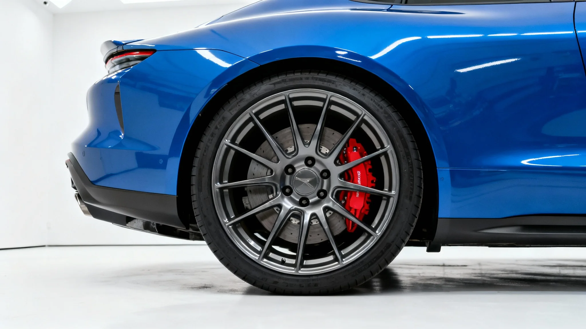 A close-up of a modern blue sports car on a white background, highlighting its custom gunmetal grey wheel with perfect flush fitment against the fender.