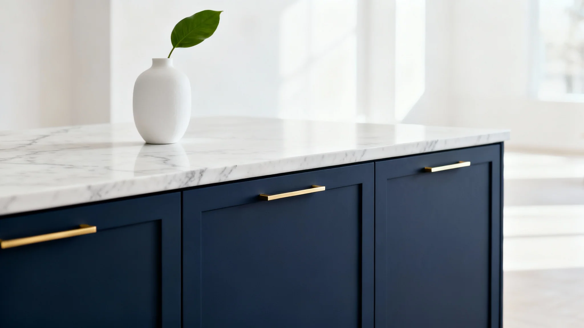 A close-up of modern, navy blue kitchen cabinets with minimalist gold handles, set against a clean white quartz countertop.