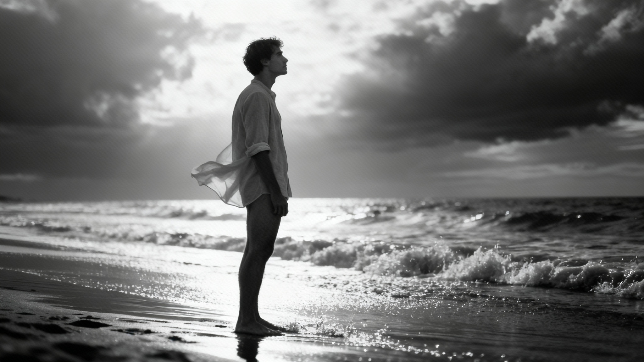 A dramatic, professional black and white photo of a man standing on a beach, looking out at the ocean. The image is a polished final result of a portrait filter.
