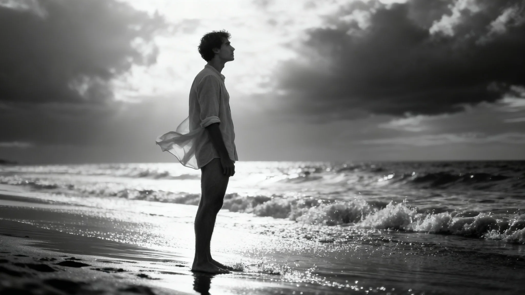 A dramatic, professional black and white photo of a man standing on a beach, looking out at the ocean. The image is a polished final result of a portrait filter.