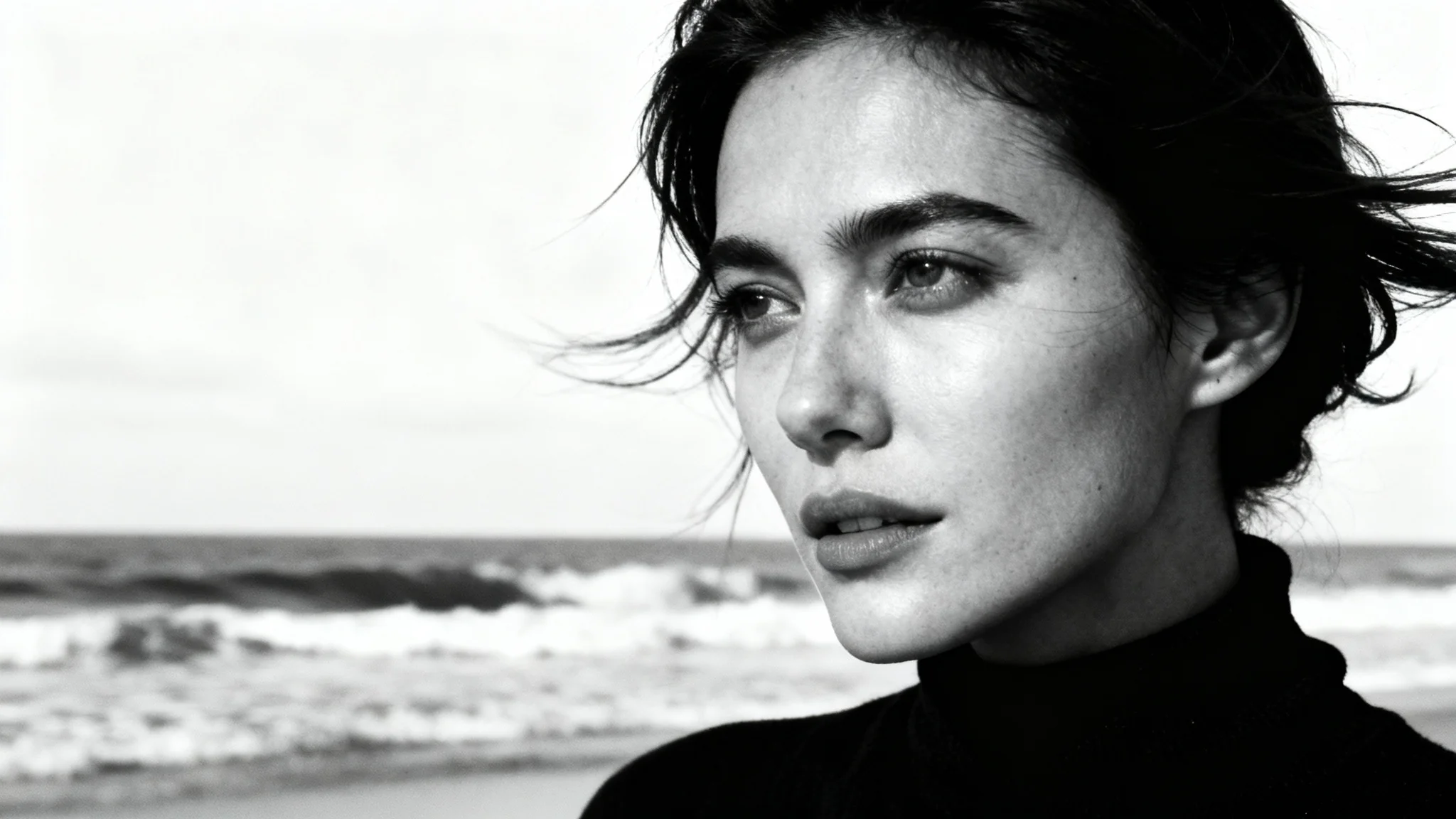 A striking black and white portrait of a woman on a beach, with windswept hair and a serene expression, presented as a photo print against a white background.