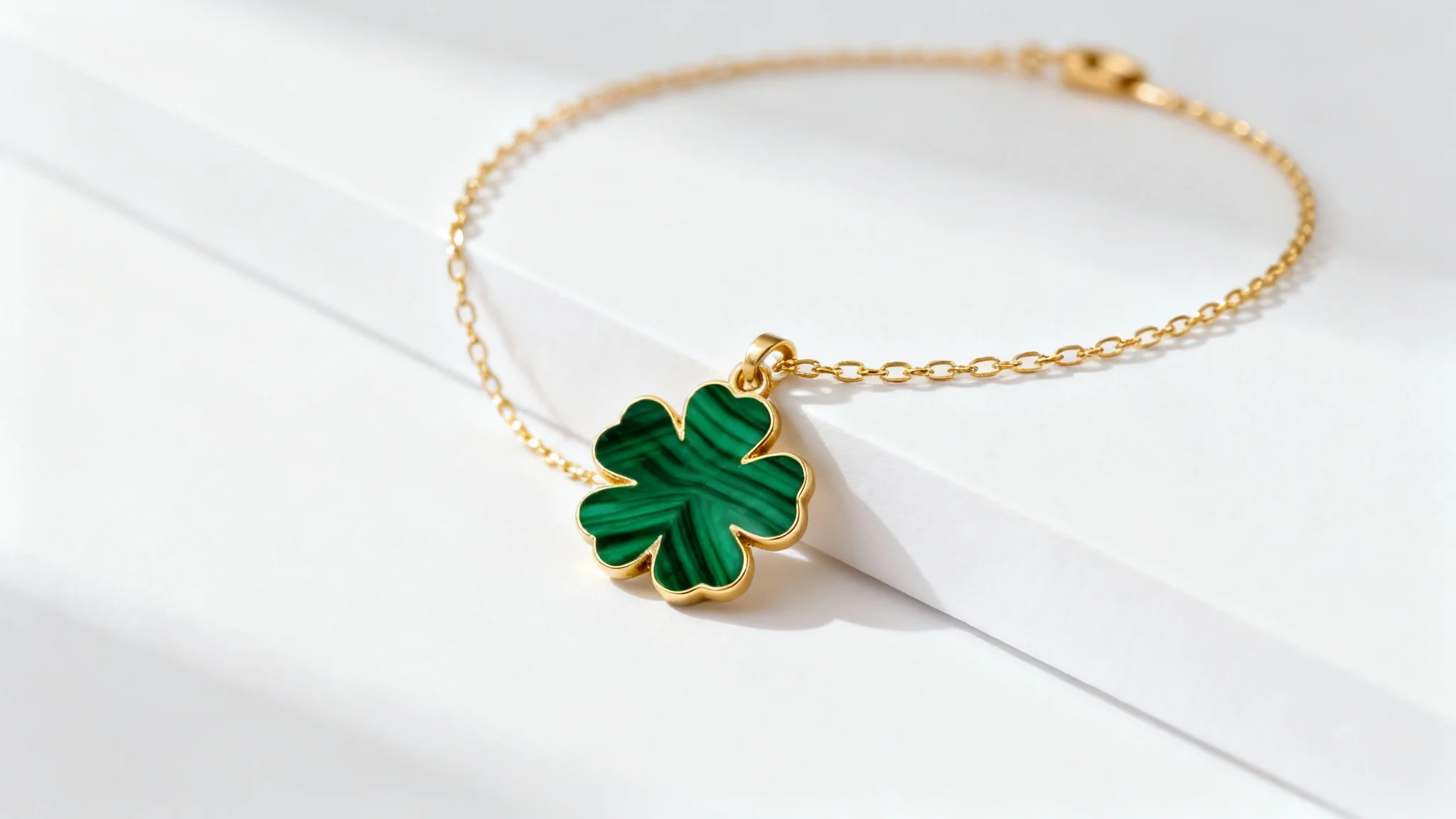 An elegant, delicate gold bracelet featuring a single green malachite four-leaf clover charm, displayed on a clean white background in a professional product shot.