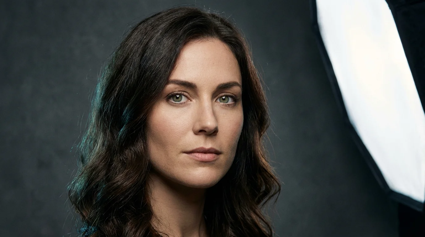 A realistic studio portrait of a woman with wavy brown hair and green eyes, looking at the camera against a dark gray background.