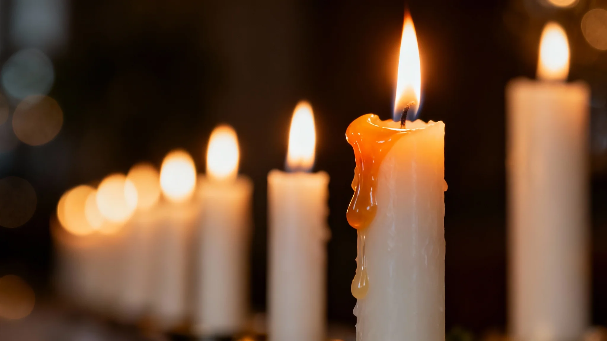 A close-up, photorealistic shot of lit white candles, with a dreamy, out-of-focus background of warm golden bokeh lights creating a serene atmosphere.