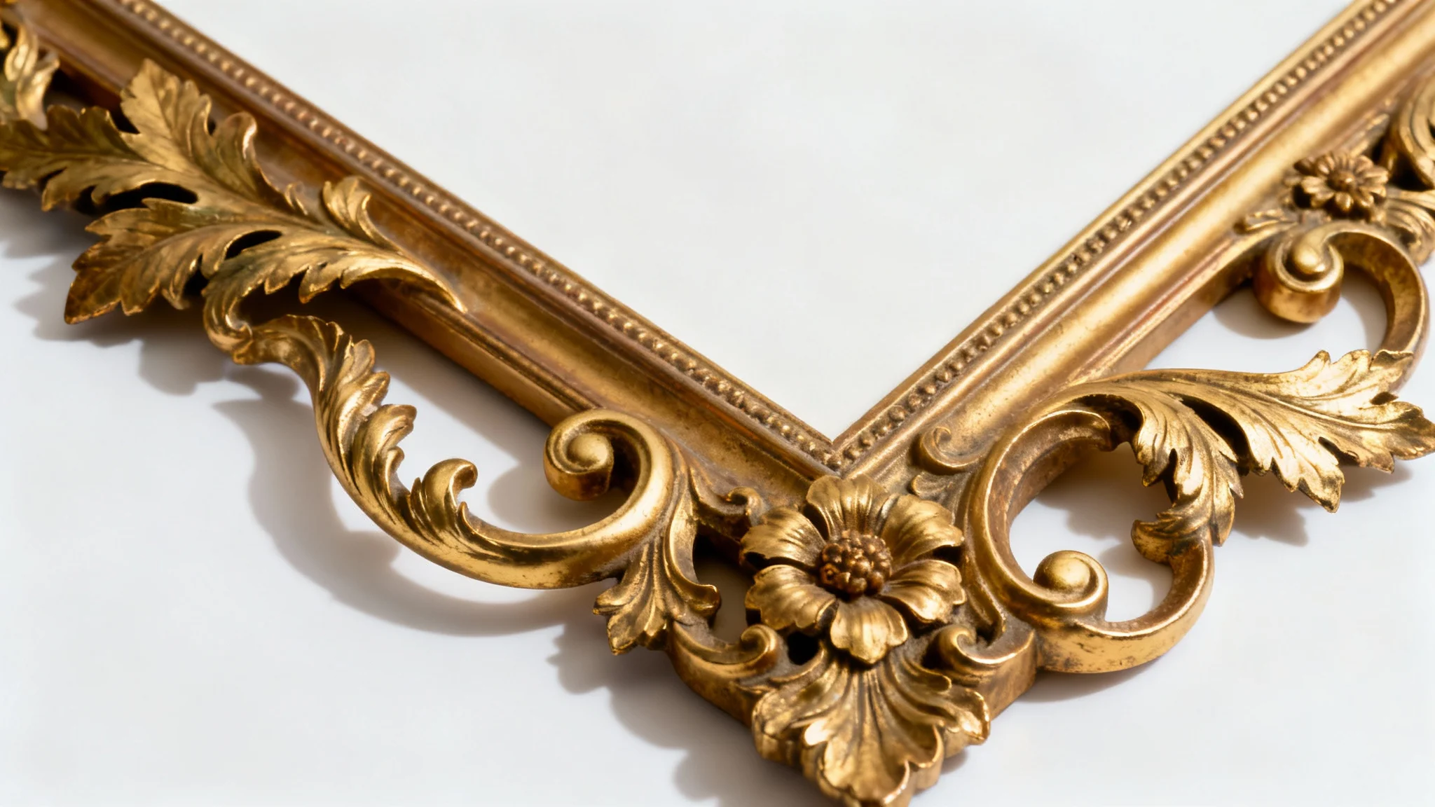 A close-up of an ornate, empty Rococo-style picture frame, featuring intricate gold-gilded carvings of leaves and scrolls, set against a plain white background.