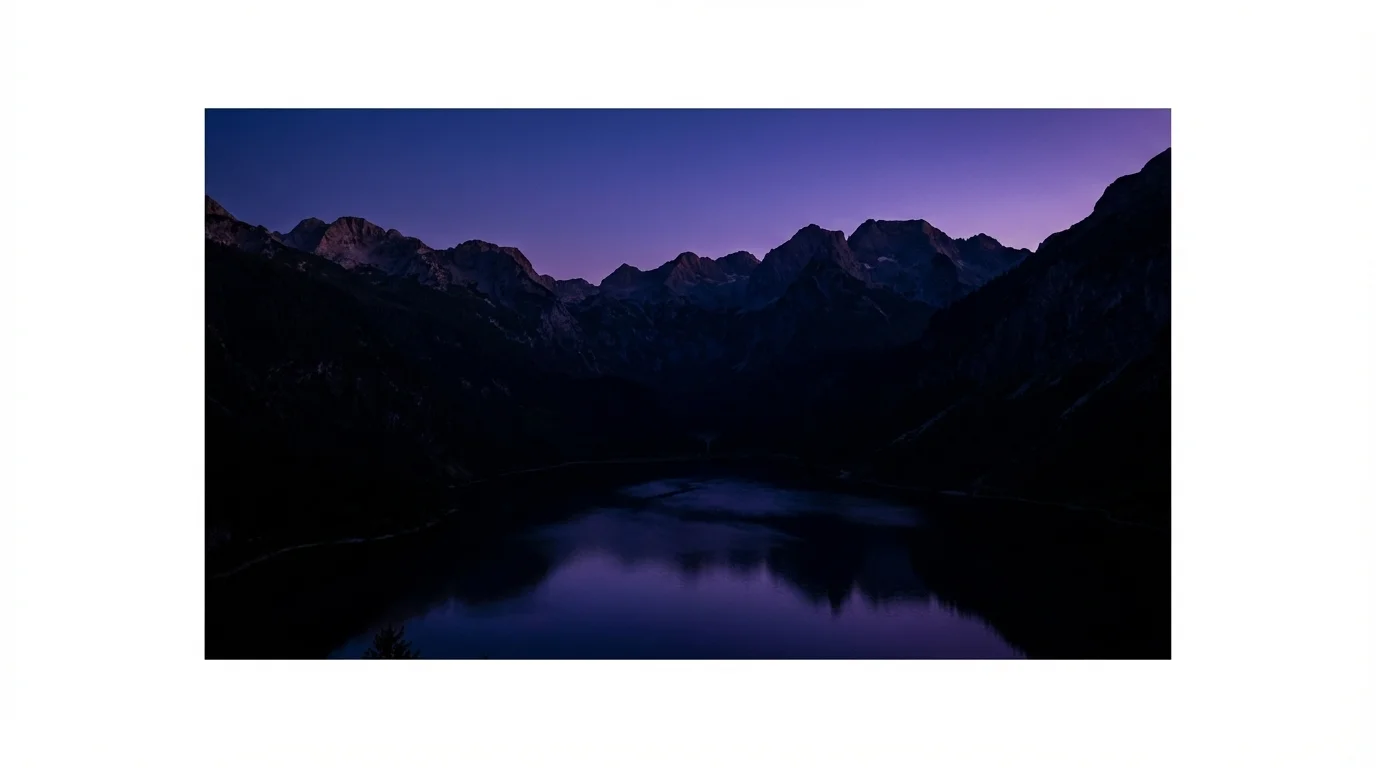 A dark and moody 16:9 photograph of a mountain landscape at dusk. The brightness has been reduced for a dramatic, atmospheric effect, showing deep shadows and a rich, dark color palette.