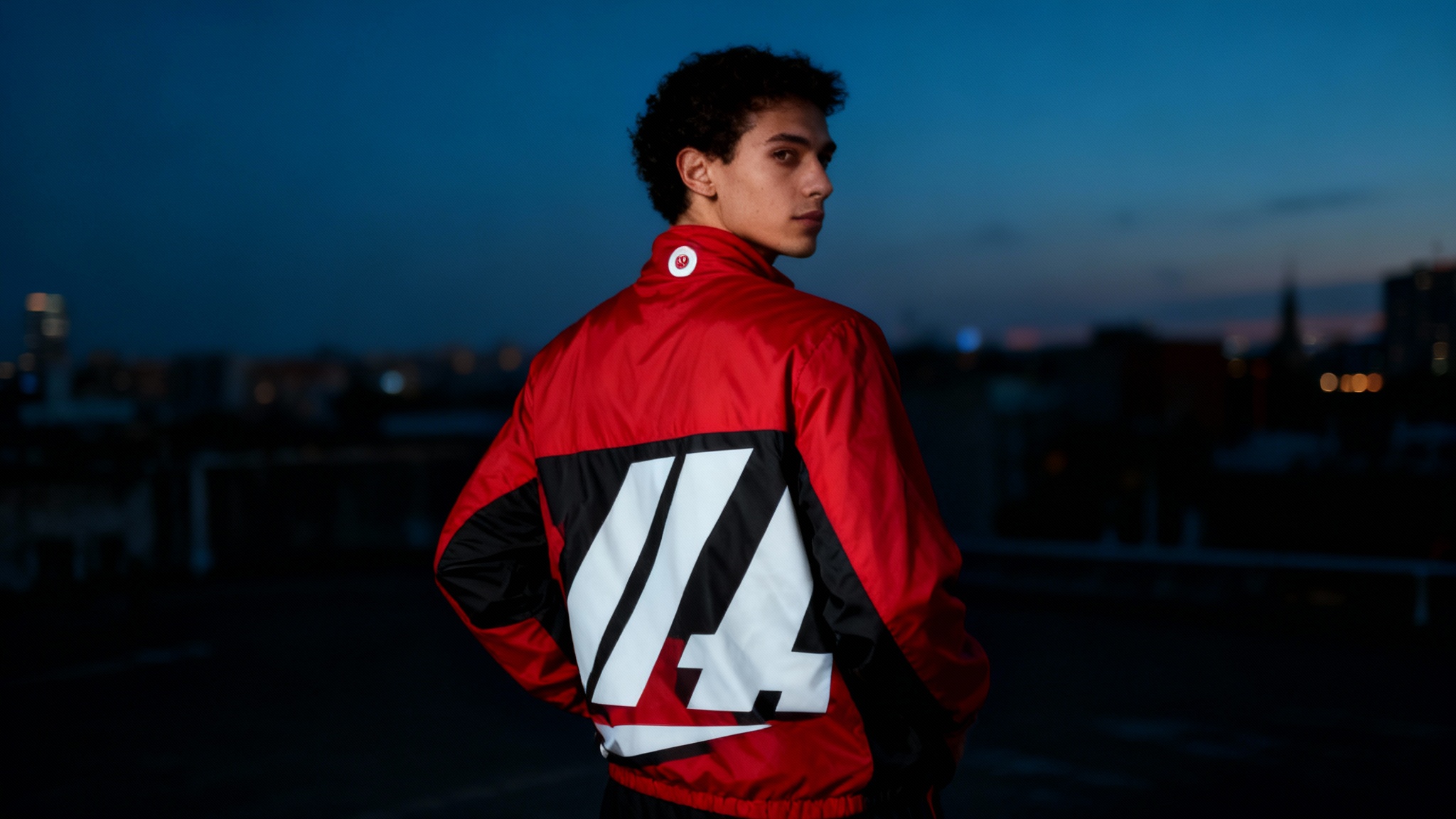 A model wears a custom-designed vibrant red windbreaker jacket with black accents, showcasing a large graphic on the back in a stylish urban setting.