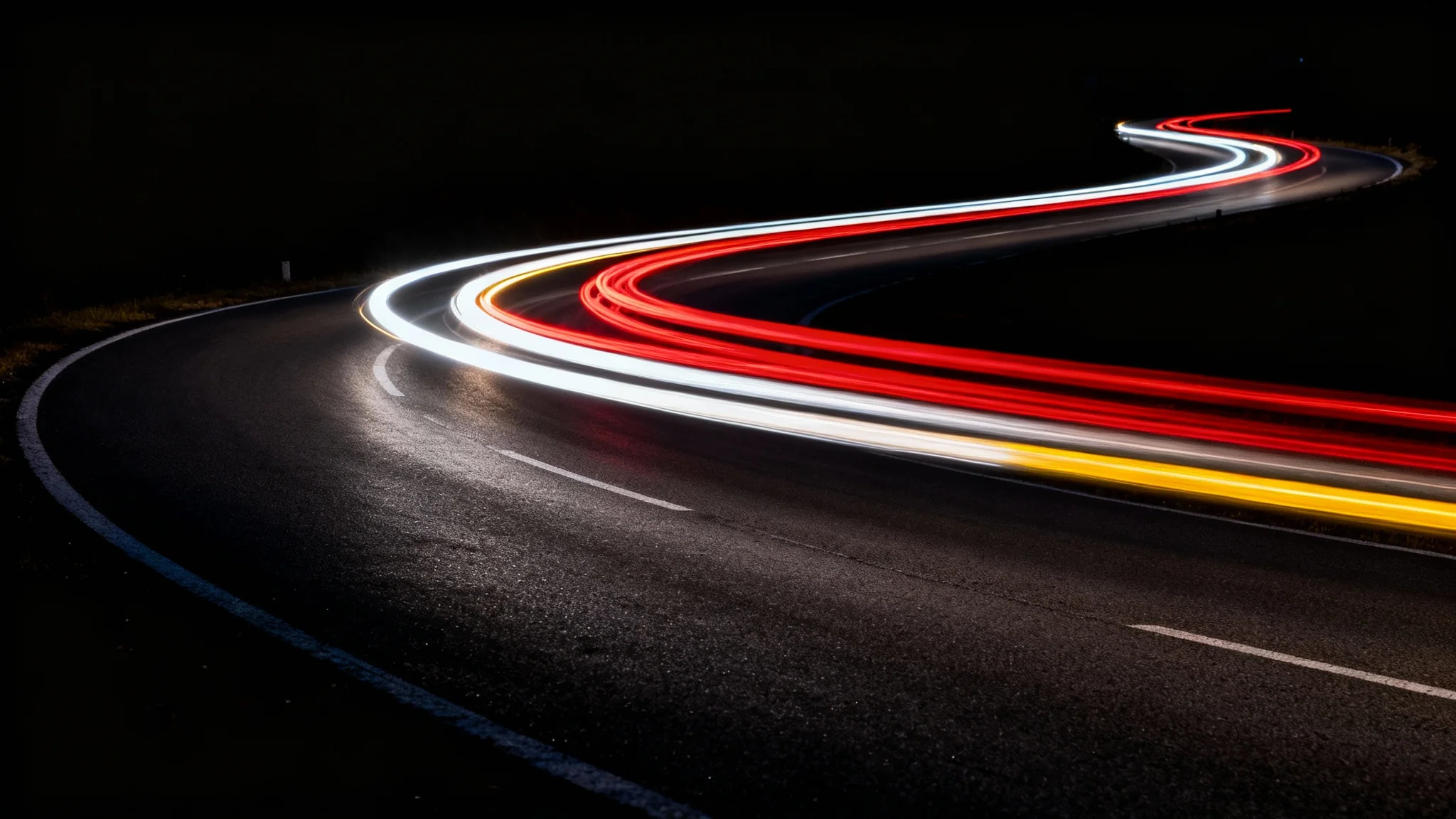A dramatic long-exposure photograph capturing vibrant red and white light trails from moving cars on a winding road at night, creating a sense of speed and motion.