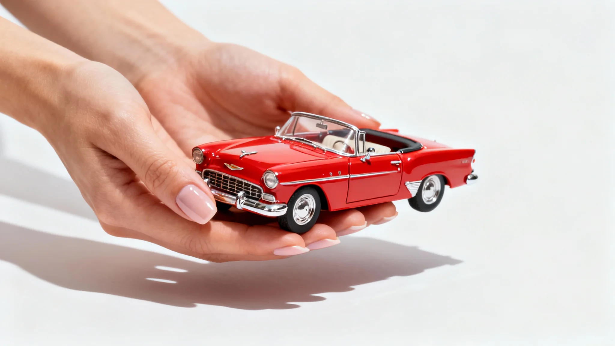 A woman's hands hold a tiny red classic car, demonstrating size illusion photography against a plain white background.