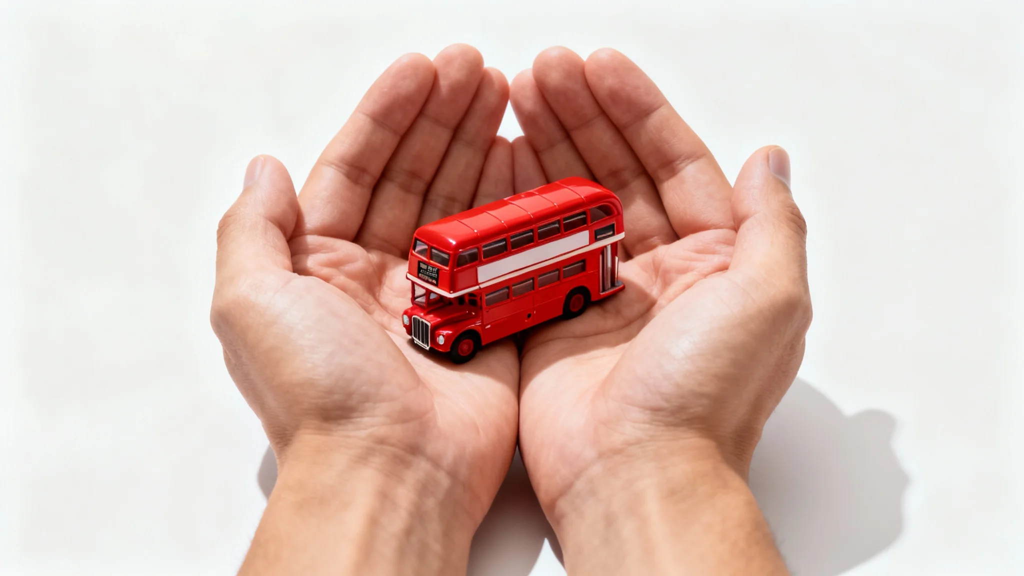 A studio photograph showing a pair of hands holding a tiny, realistic red double-decker bus, creating a playful size illusion.