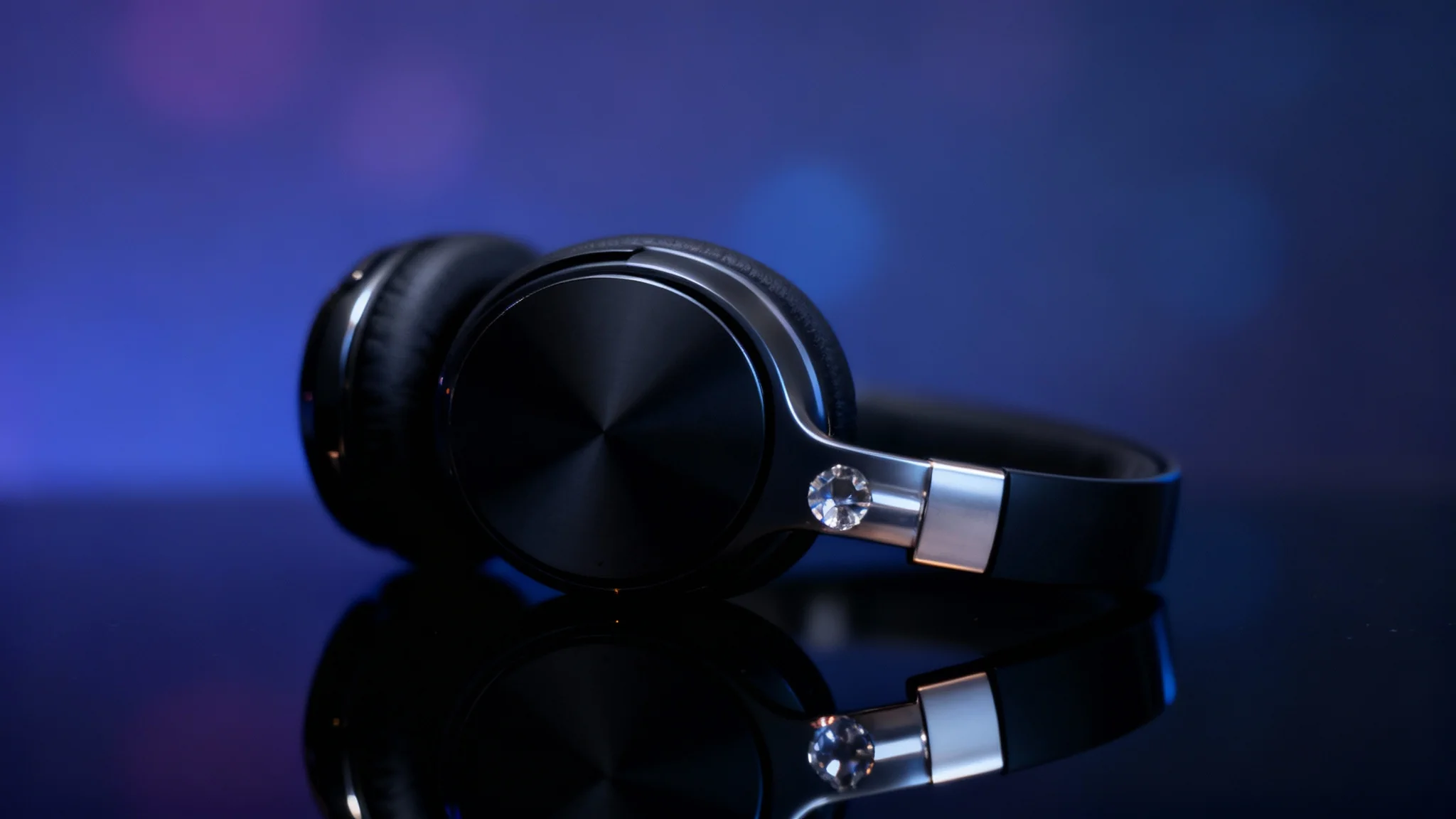 A hyper-realistic hero image showing a high-end electronic gadget on a glossy, reflective black surface, creating a perfect mirror image. The professional studio lighting highlights the product's sleek design against a blurred blue and purple background.