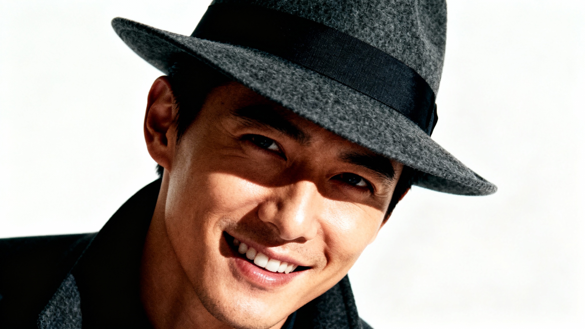 A dramatically edited, high-fashion portrait of a person wearing a dark grey fedora against a clean white background, showcasing advanced photo editing effects like high contrast and cinematic lighting.