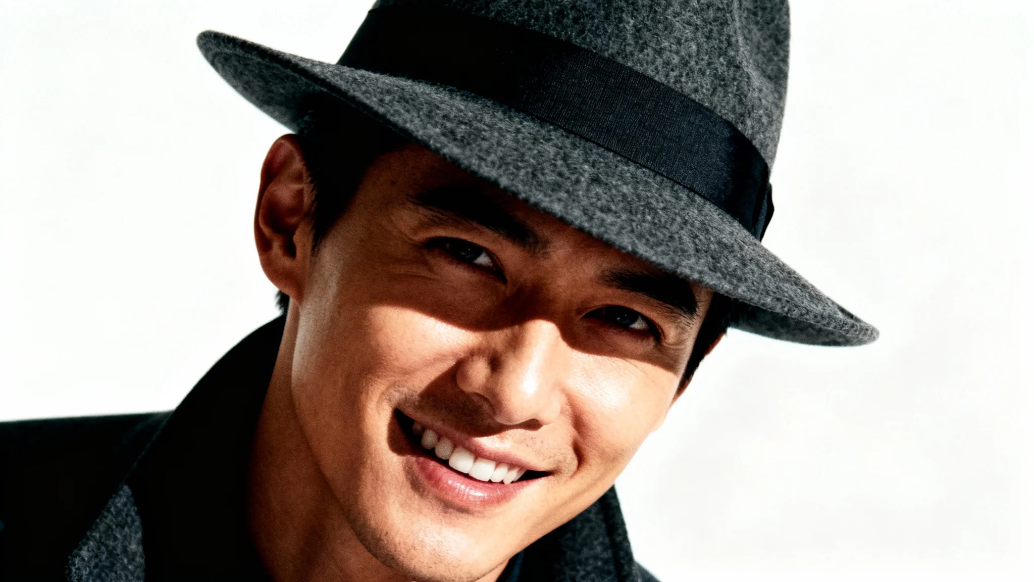 A dramatically edited, high-fashion portrait of a person wearing a dark grey fedora against a clean white background, showcasing advanced photo editing effects like high contrast and cinematic lighting.