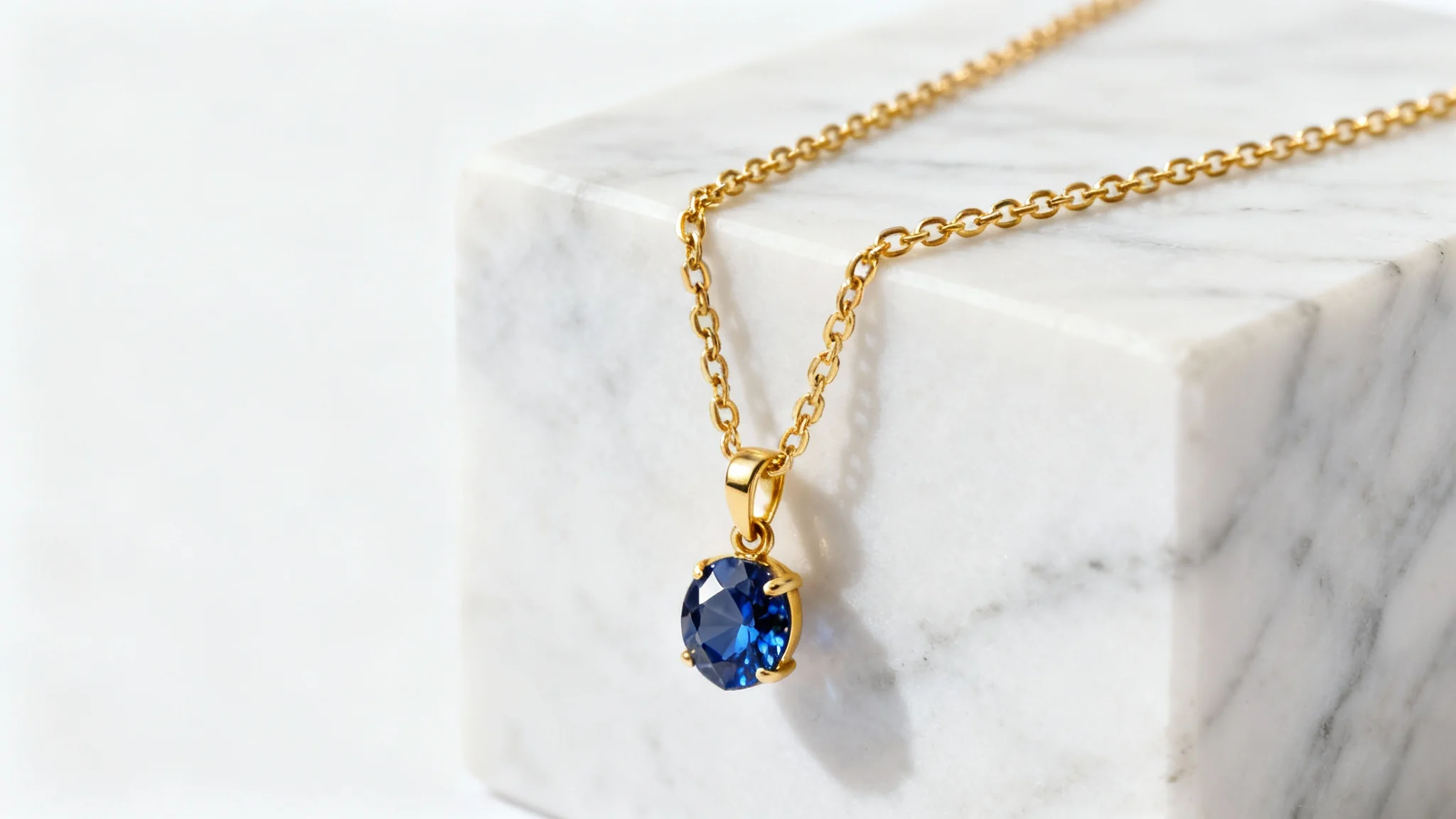 A professional studio photograph of a beautiful gold and sapphire necklace elegantly displayed on a white marble block against a clean white background.