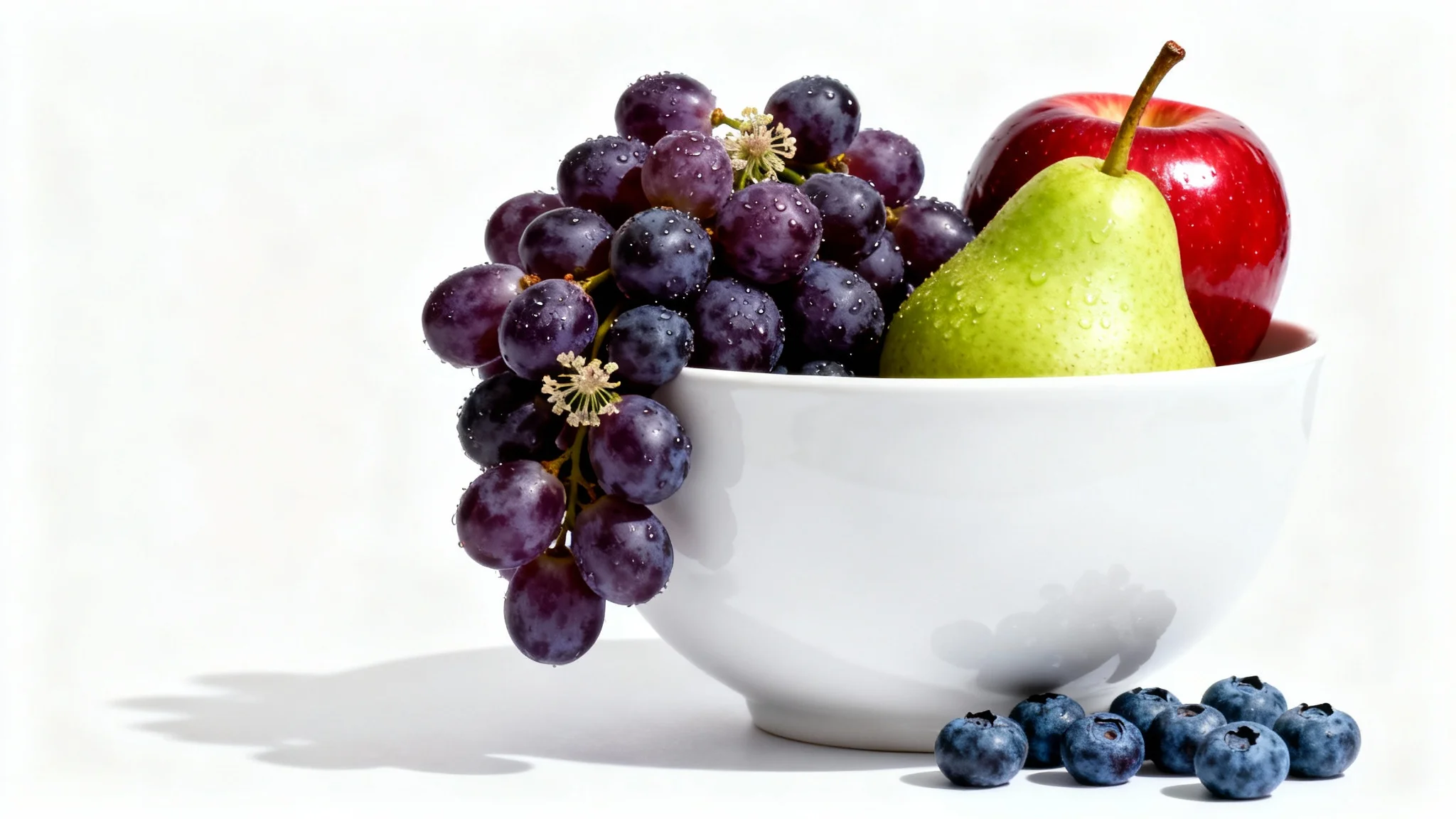A modern still life photo of a white ceramic bowl filled with fresh grapes, a red apple, and a green pear, shot in a studio setting against a pure white background.