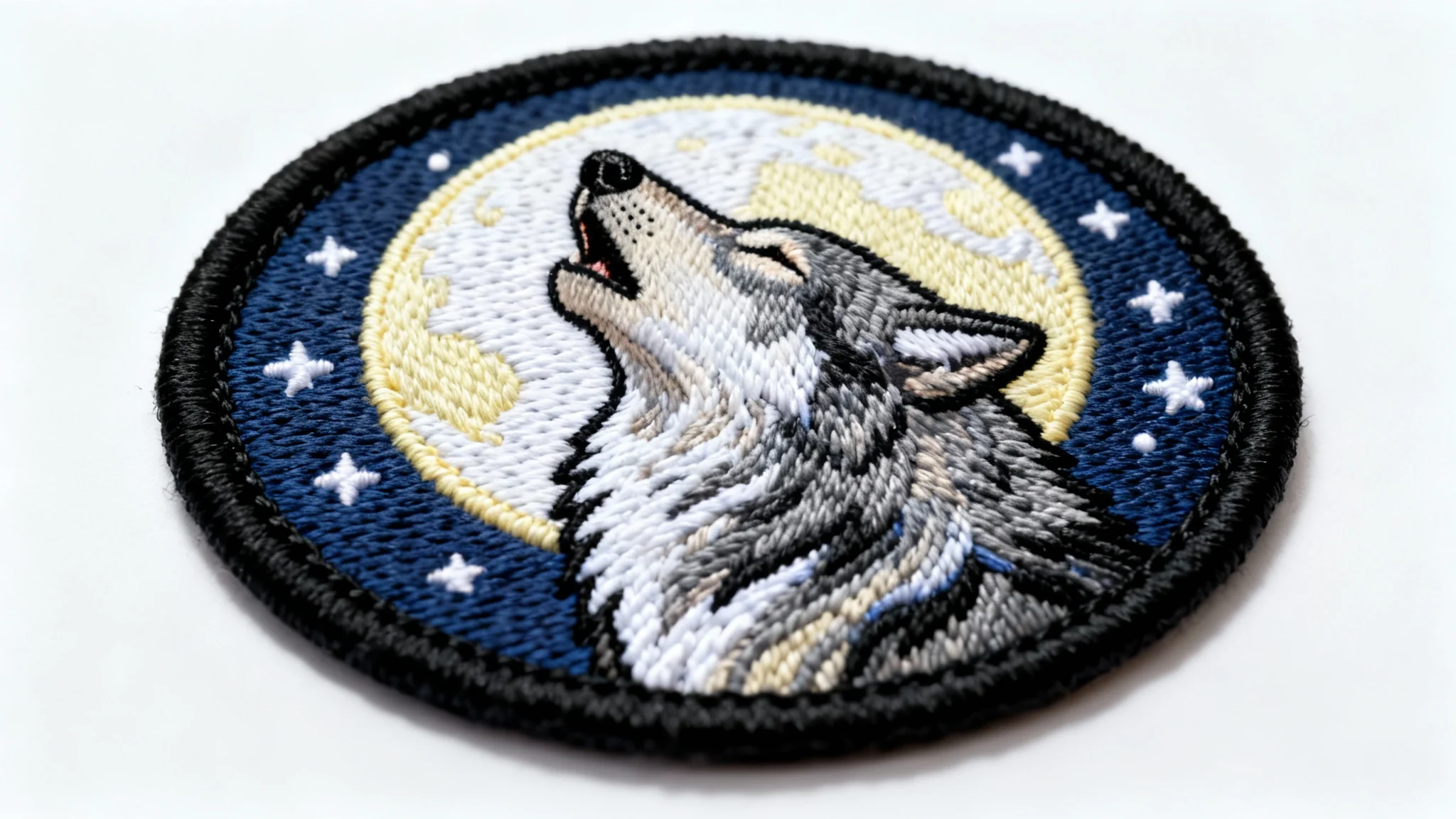 A photorealistic mockup of a round embroidered patch on a white background, featuring a detailed design of a grey wolf howling at a full moon.